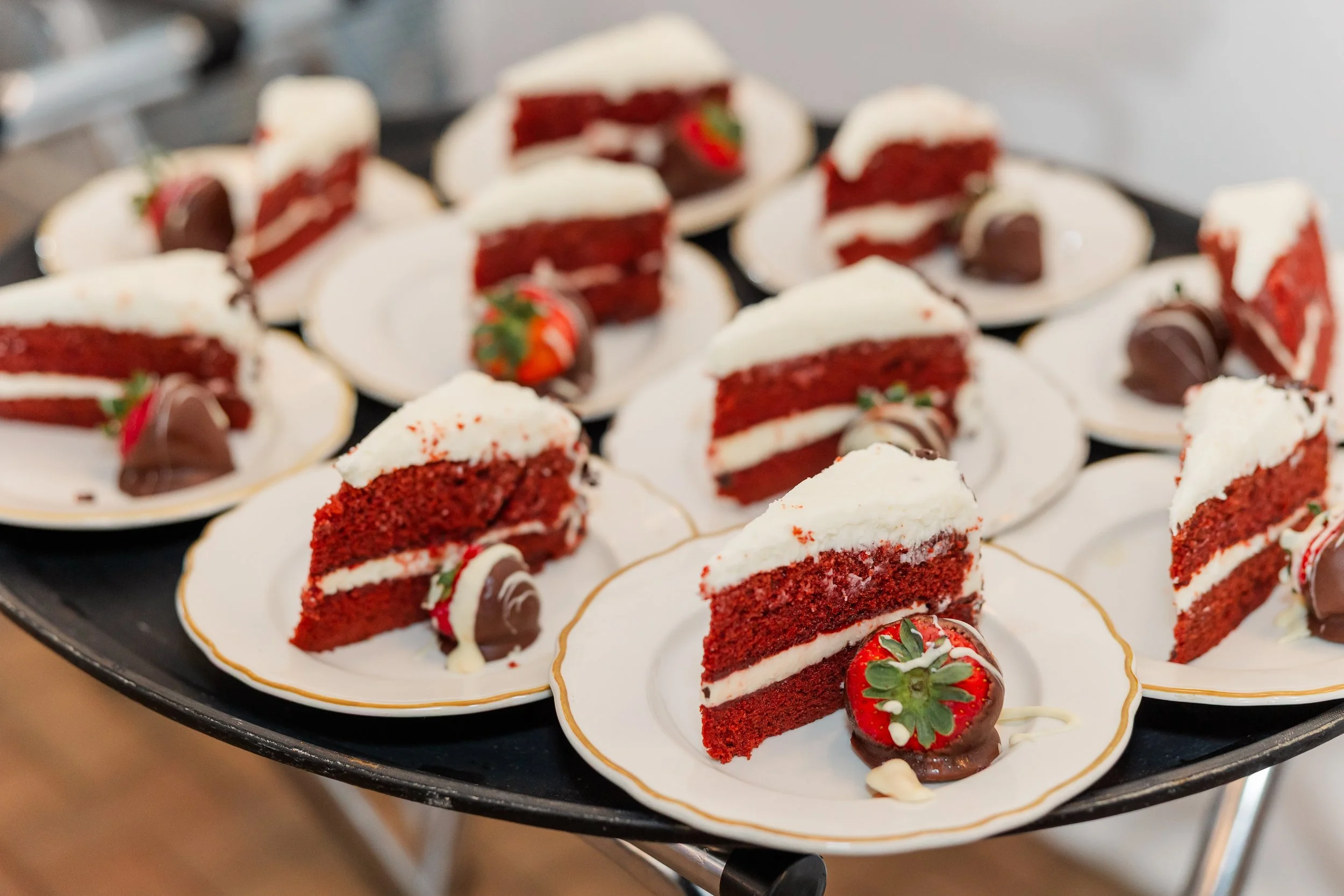 Plate of red velvet cake slices with cream cheese frosting, strawberries, and chocolate decorations on plates.