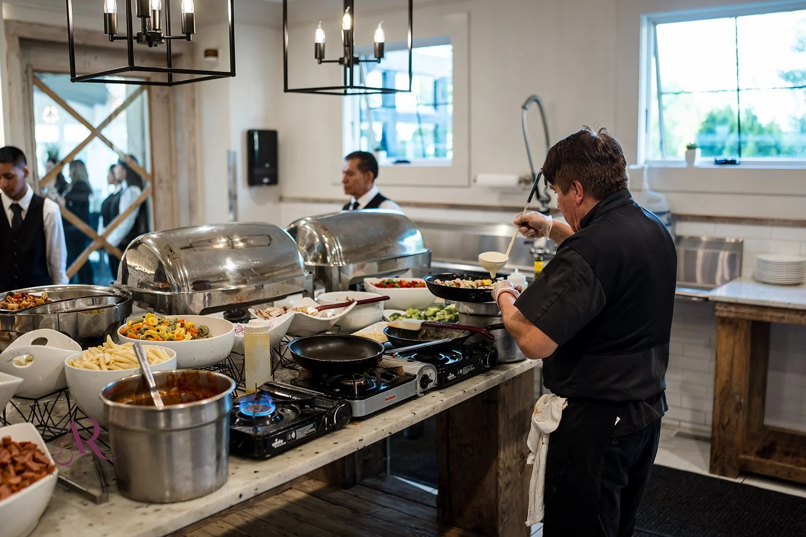 Chef preparing food at a buffet station, with multiple bowls of pasta and salad dishes, in a restaurant kitchen.