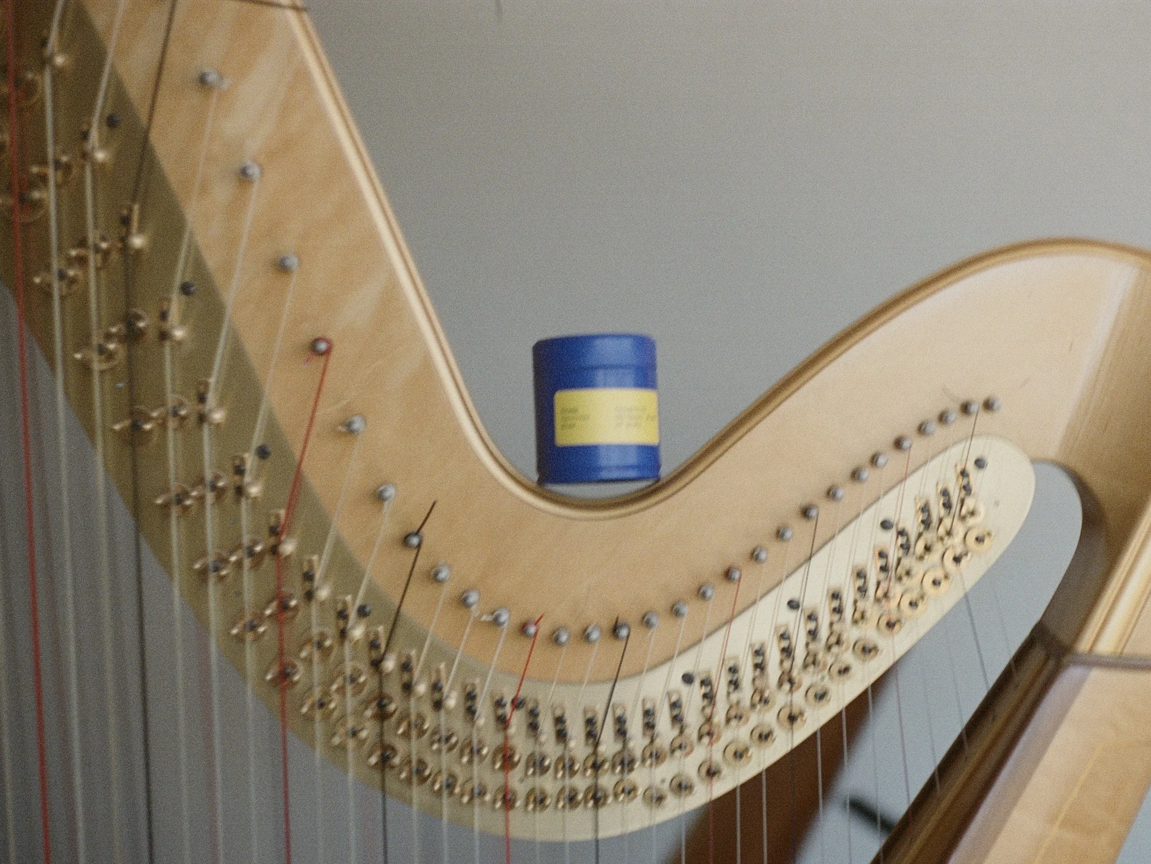 Close-up view of the inside of a classical guitar, showing the soundboard, strings, bridge, and tuning pegs, with a blue can of spray adhesive placed on the guitar body.