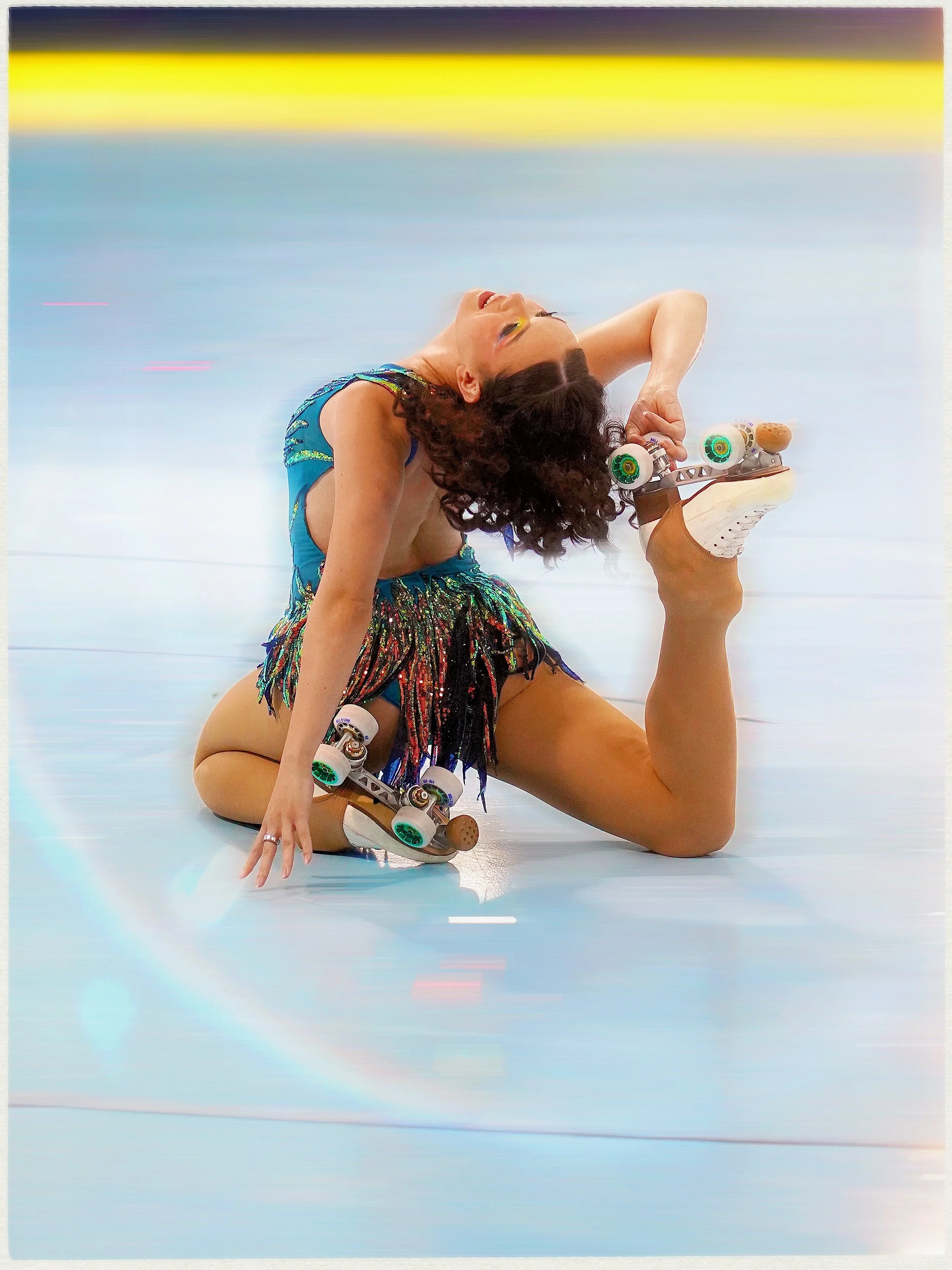 A woman performing a yoga pose on a roller skate with rainbow-colored makeup and a colorful outfit.