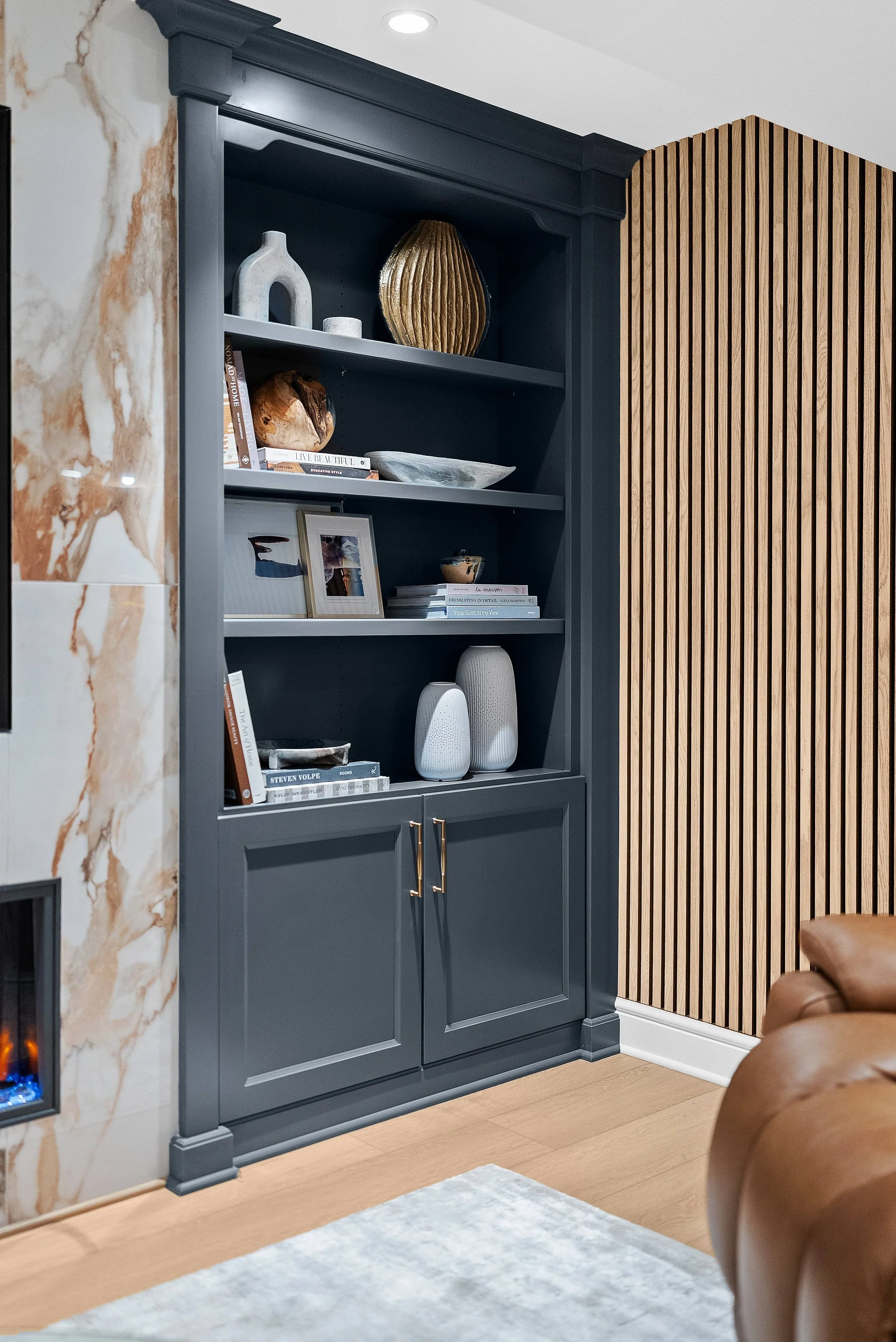 A dark blue bookshelf with decorative items, books, and a framed photo on four shelves, next to a wood-paneled wall and a marble surface on the left.