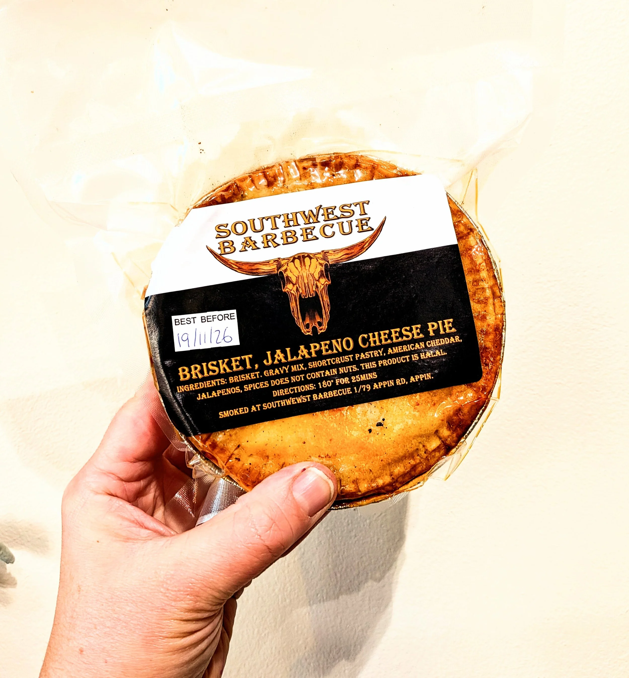 A person holding a packaged beef jalapeno cheeseburger pie from Southwest Barbecue, with a label showing the best before date of 19/11/26.