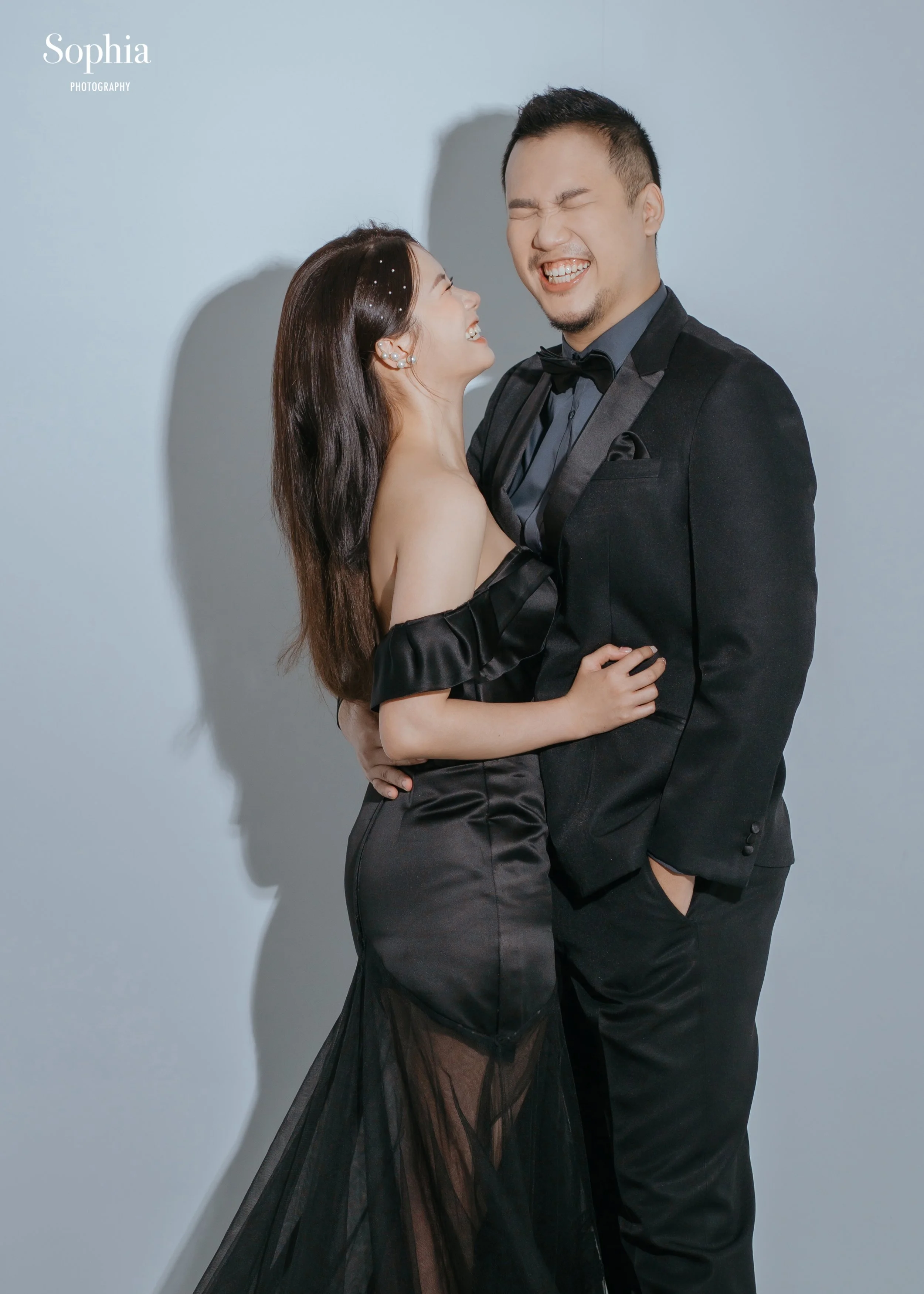 簡約棚拍婚紗攝影，新人穿著黑色禮服與西裝自然相視而笑
