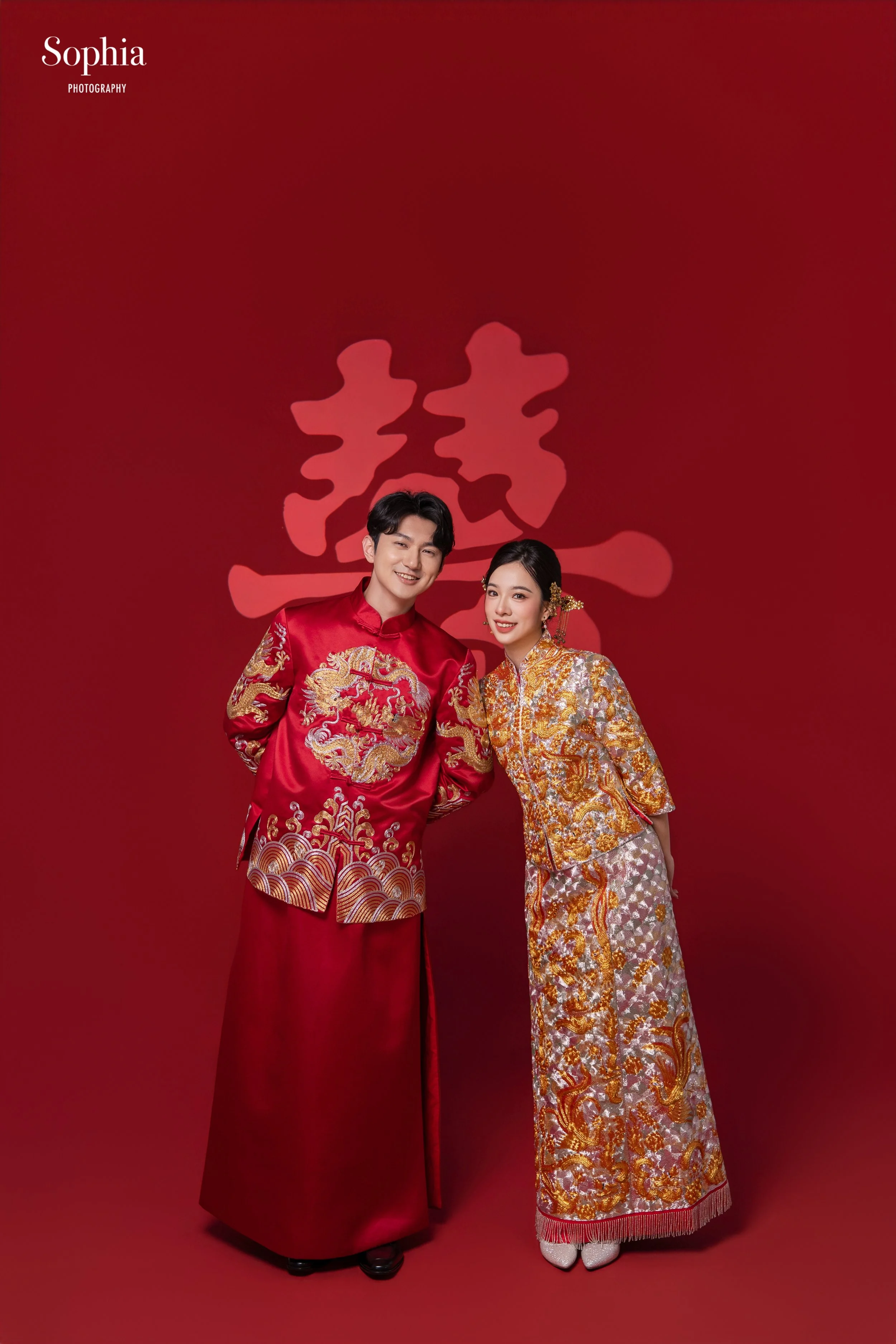 中式婚紗攝影，新人穿著紅色傳統中式禮服於紅色背景前合影