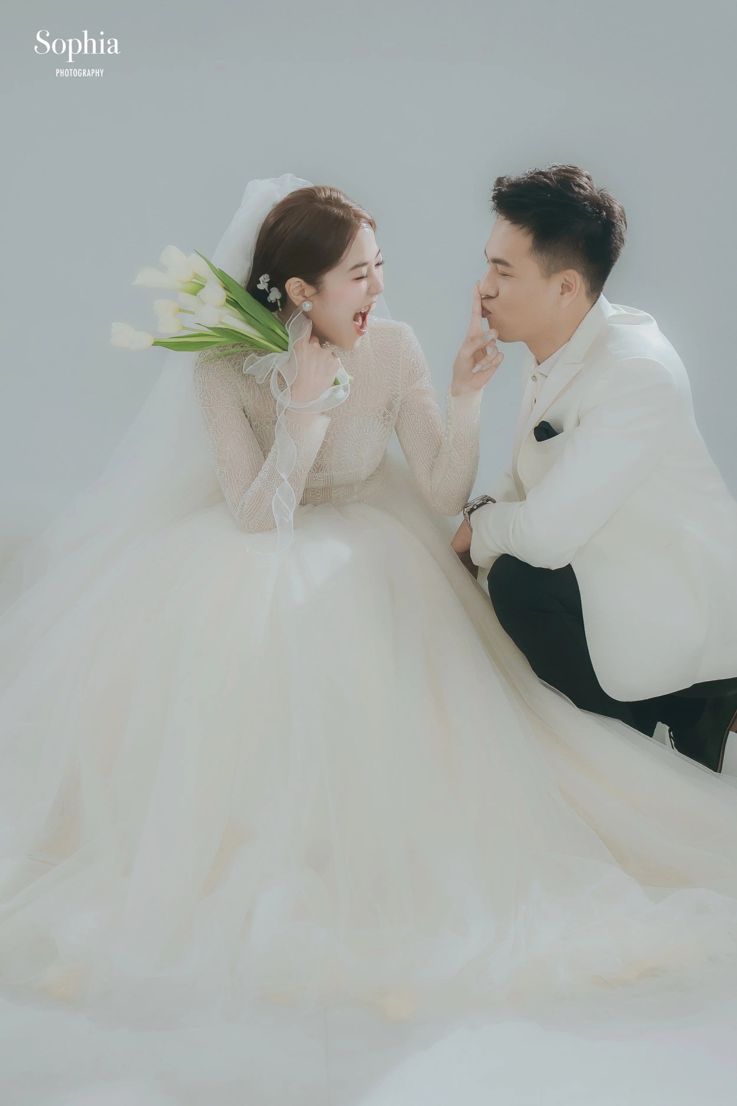 簡約棚拍婚紗攝影，新人穿著白紗與白色西裝坐姿自然互動
