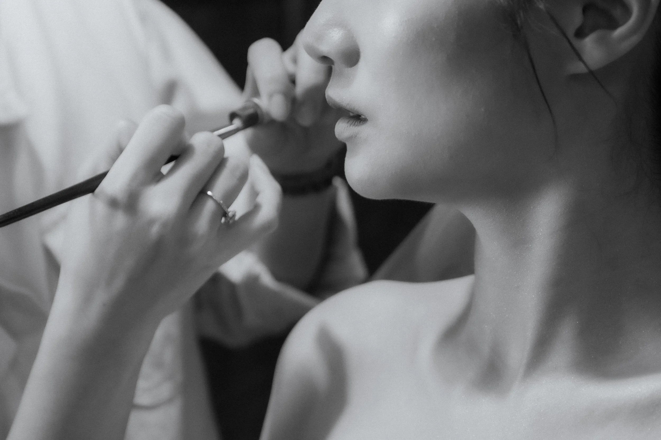 Close-up of a woman applying lipstick with her eyes closed, in black and white.