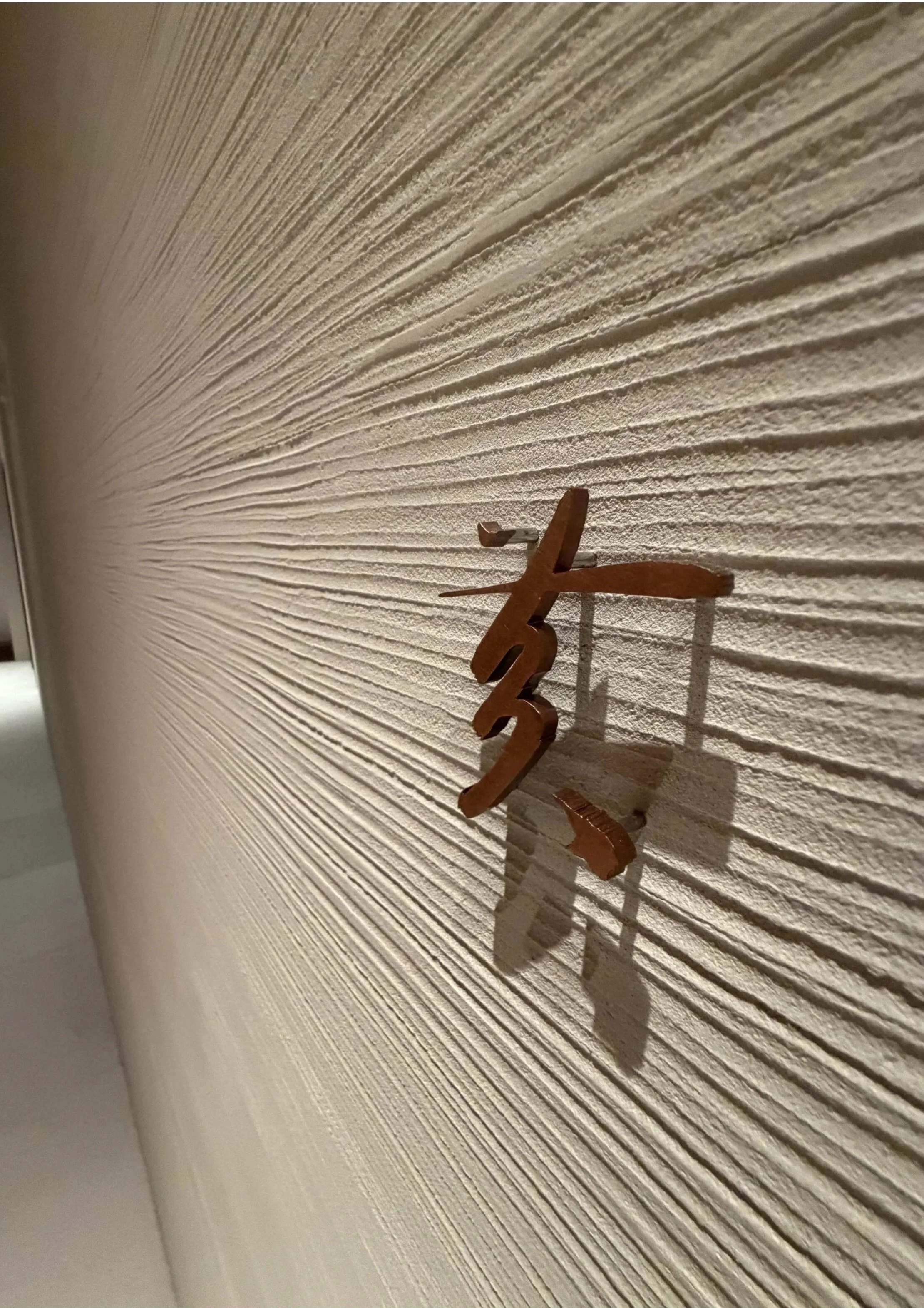 Close-up of a textured beige wall with an orange-brown decorative element casting a shadow.