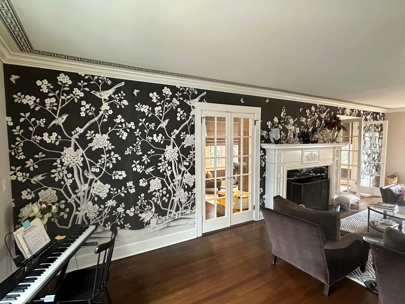Living room with black and white floral wallpaper, white fireplace mantel, piano, and seating area.