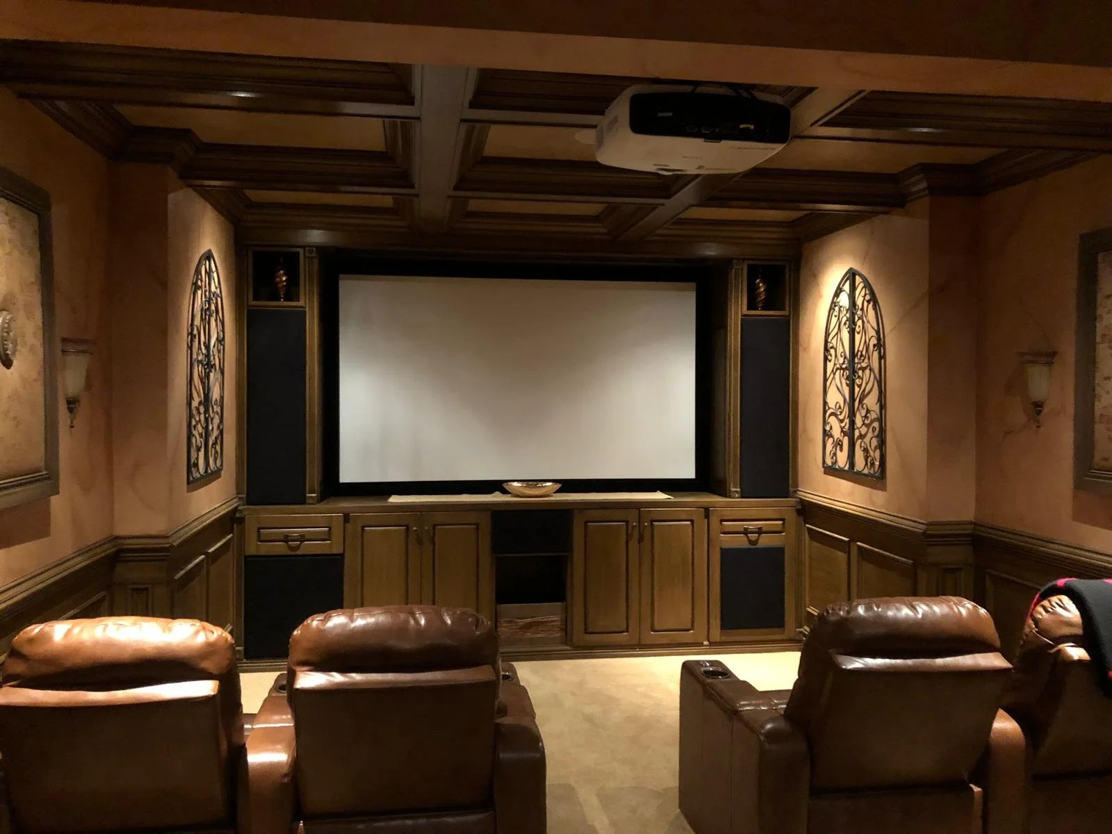 Home theater room with a large projection screen, brown leather recliners, wood-paneled walls, and decorative iron wall art.