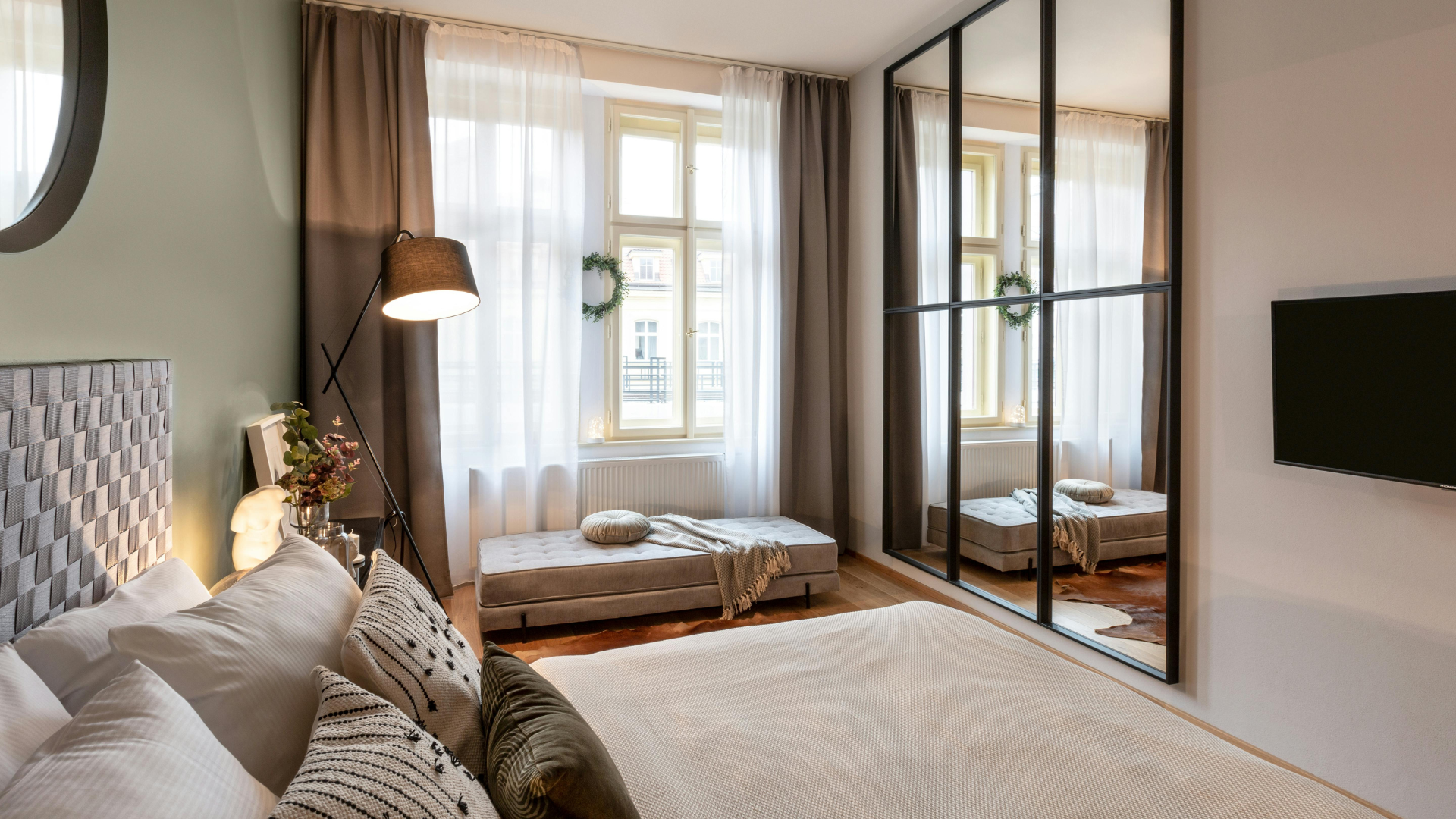 Bright modern bedroom with soft neutral furnishings, large windows and mirrored wardrobe doors.