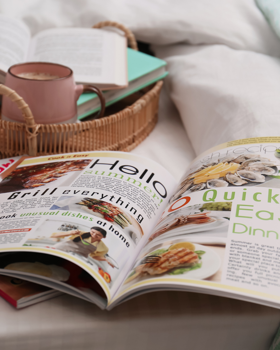 Open home and lifestyle magazine with a coffee cup and books on a soft bed.
