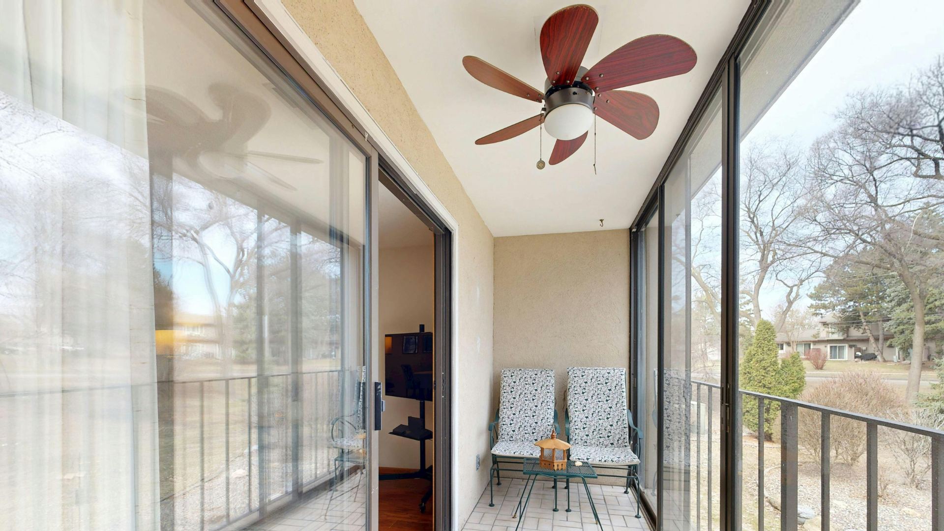 Wood-blade ceiling fan above a covered balcony with glass doors and two chairs.