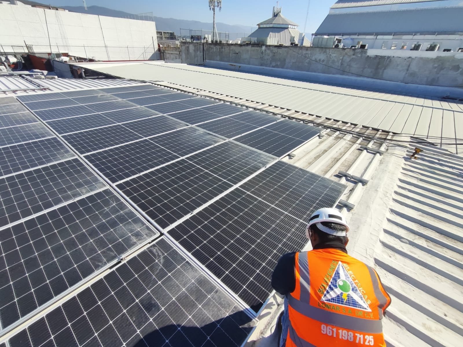 Trabajador instalando paneles solares en la azotea de un edificio con fondo de montañas y cielo despejado.