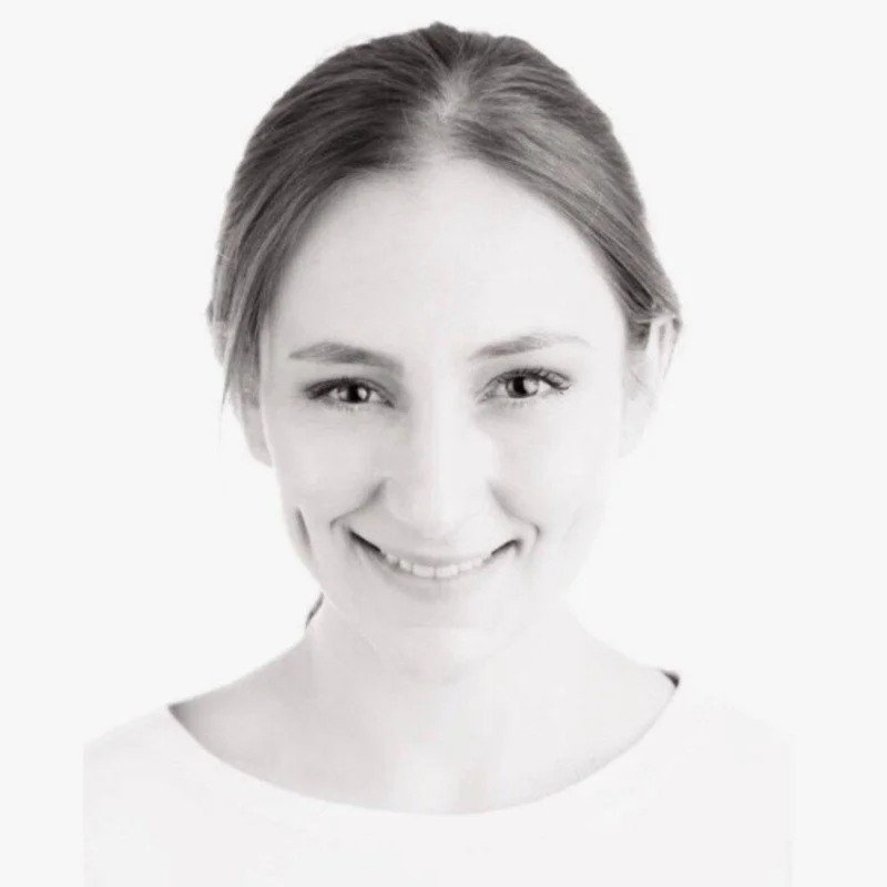 Julie Rielle - Weibliches Porträt mit freundlichem Lächeln, helles Hintergrund, elegante Frisur, sehr natürliches Make-up, welches die Gesichtszüge betont.