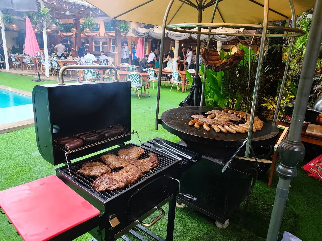 Two grills loaded with steaks, chorizo and morcilla in a garden
