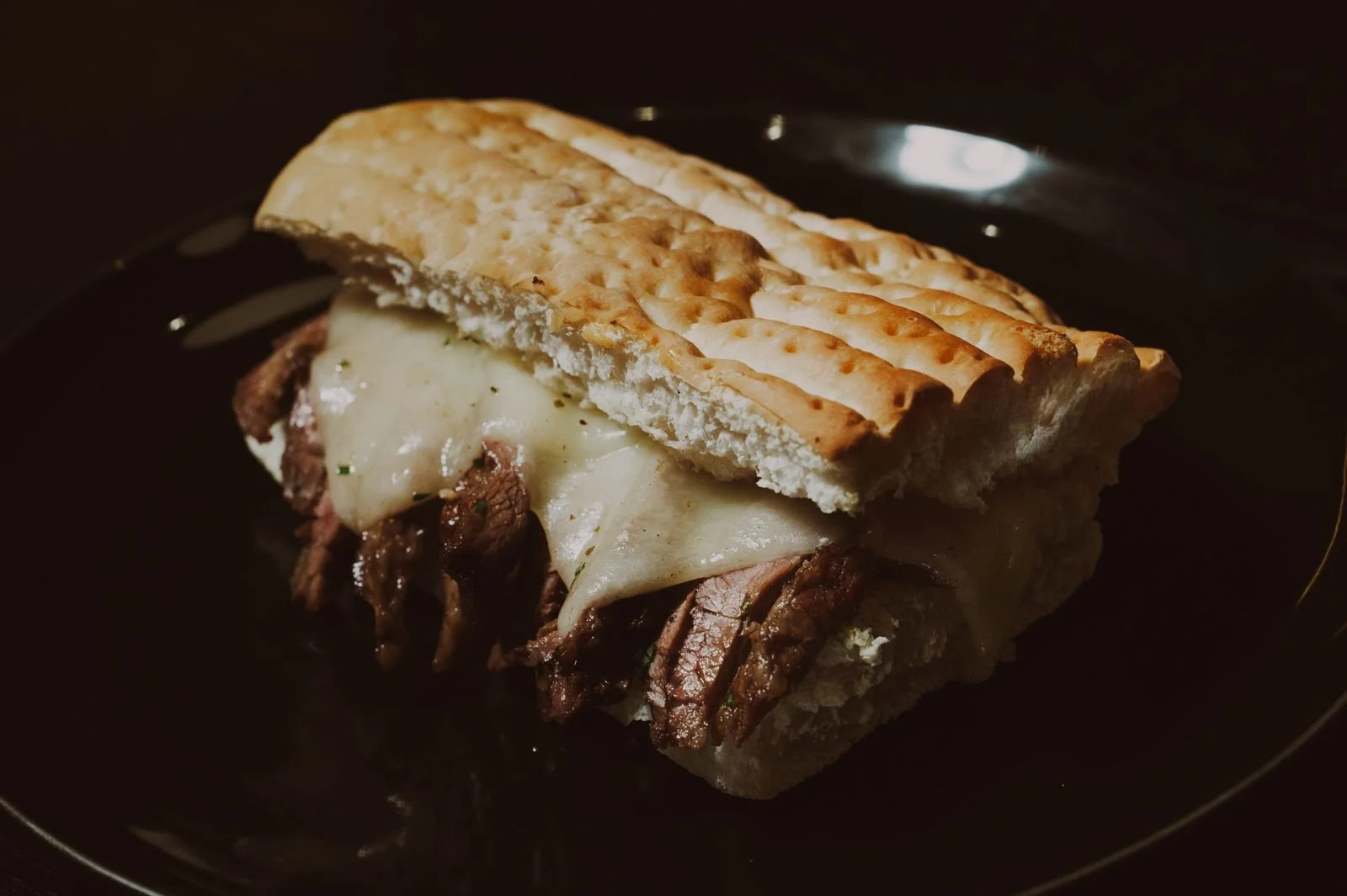 Beef sandwich with melted cheese on a dark plate