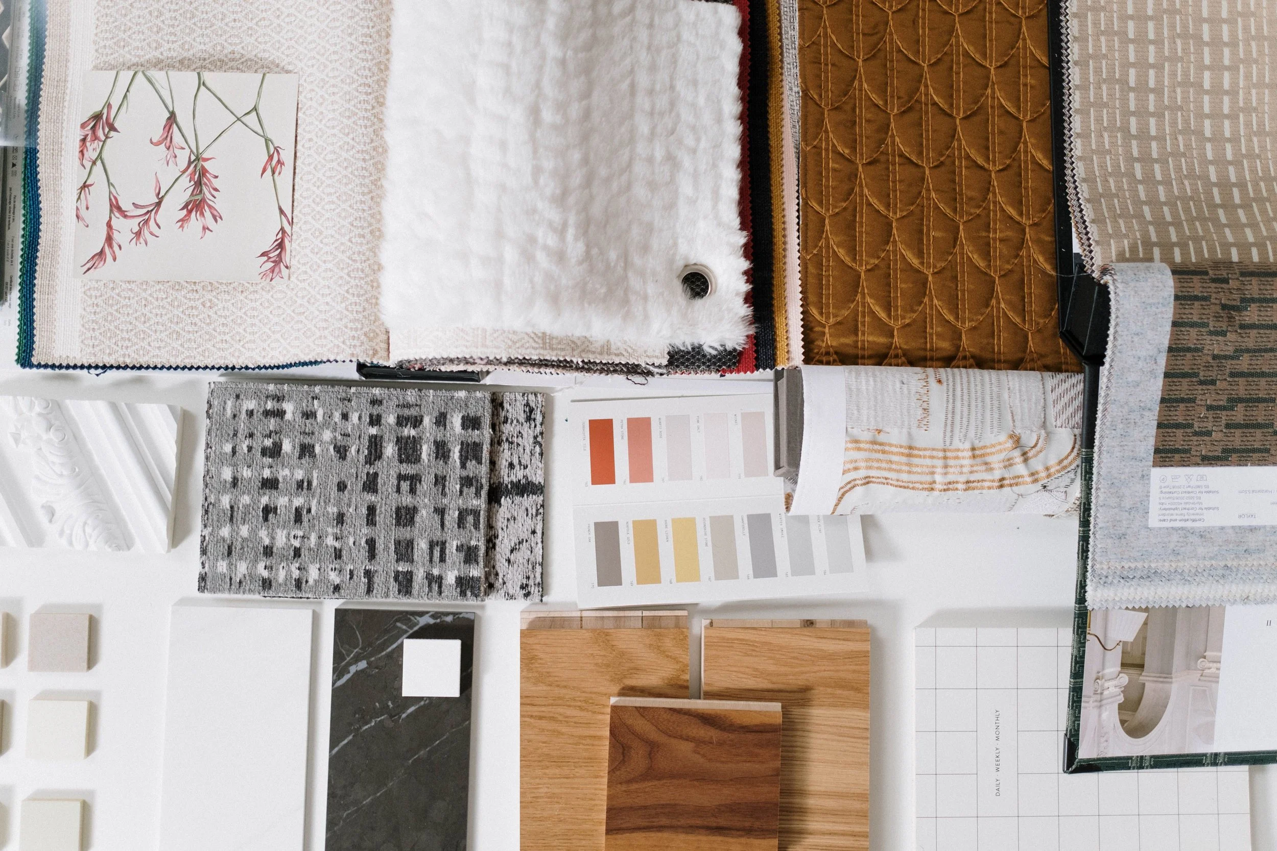 Display of various interior design materials, including rugs, fabric swatches, sample tiles, wood finishes, and a color palette chart.