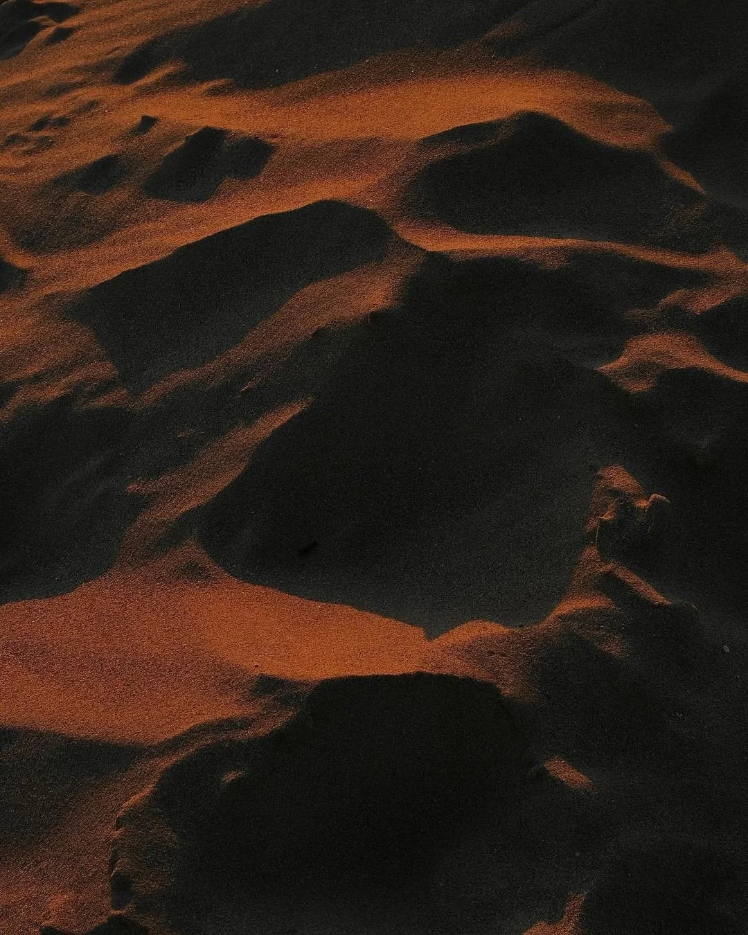 Close-up view of sand dunes at night with shadows highlighting their ridges and contours.