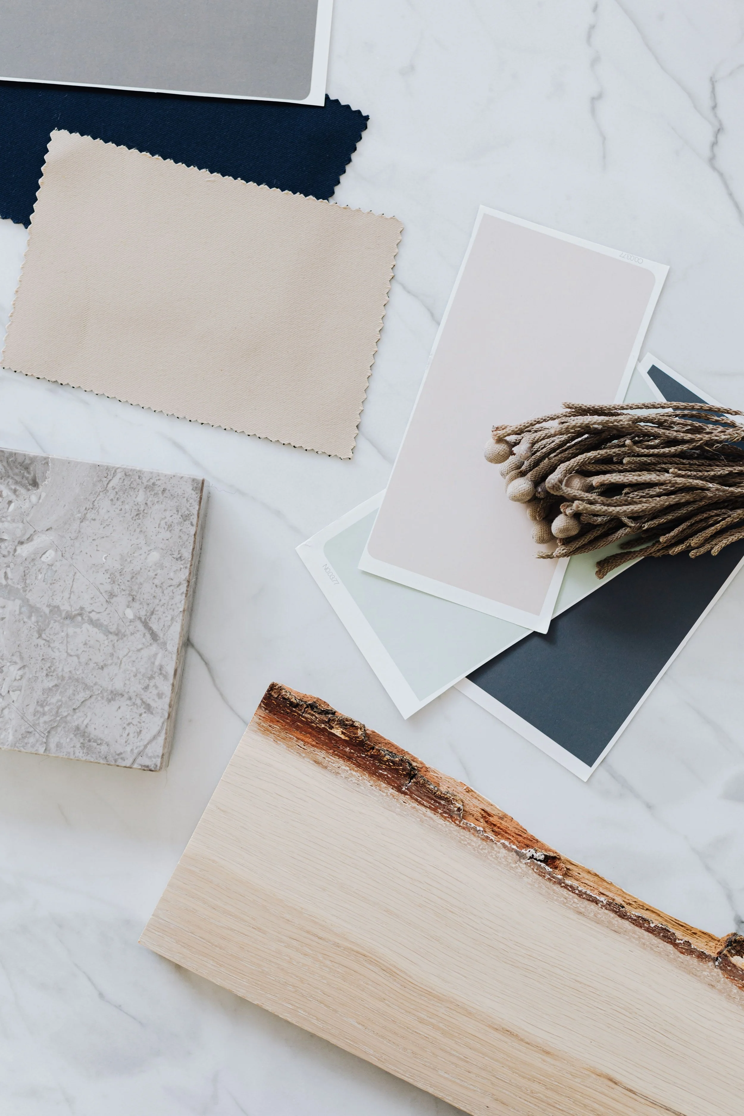 Various sample materials including fabric swatches, paint color swatches, a sample of marble, a wood sample, and a decorative textile on a white marble surface