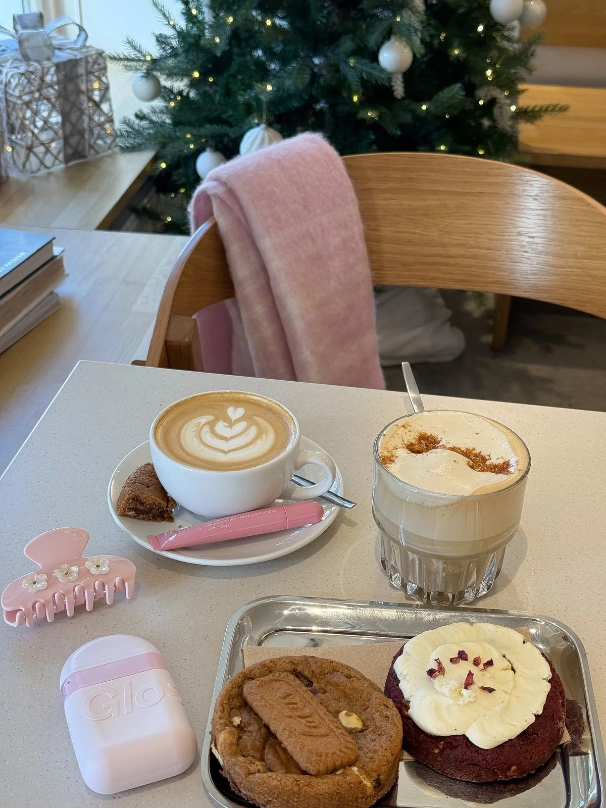 A table with coffee, dessert, and a small cookie, decorated for Christmas with a Christmas tree and gifts in the background.