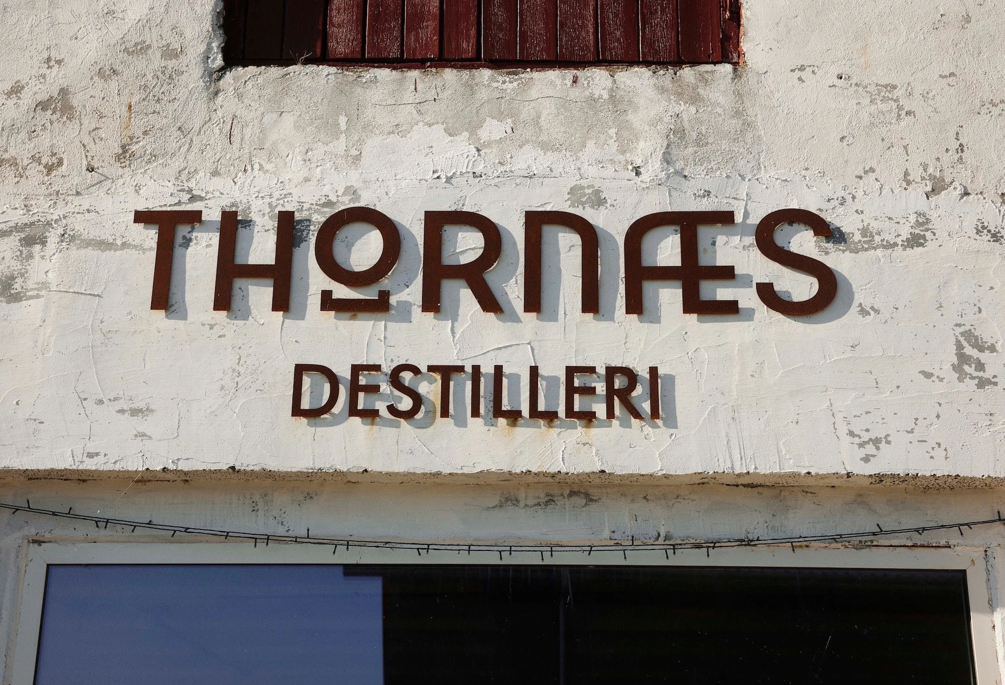 Tavle med teksten 'THORØS DESTILLERI' på en hvid, lidt slidt væg.