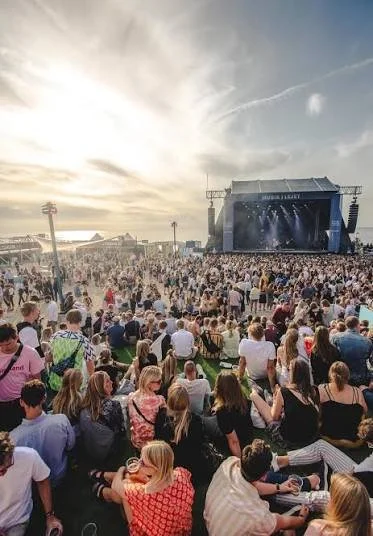 En festival-scene med en stor crowd foran en udendørs scene med musik.