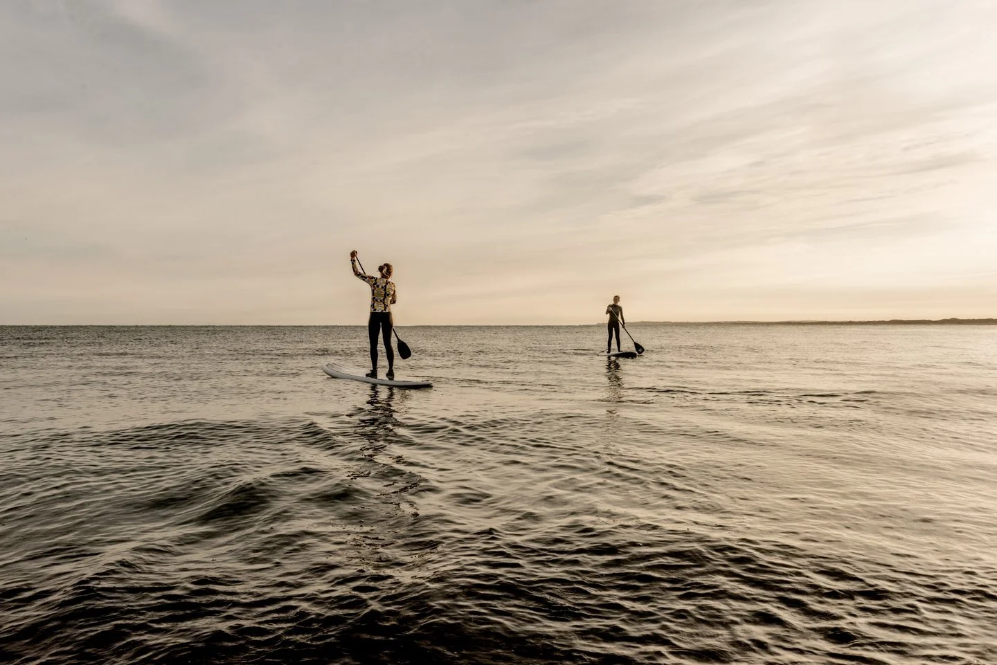 To personer der stand-up paddleboarding på havet ved solnedgang.