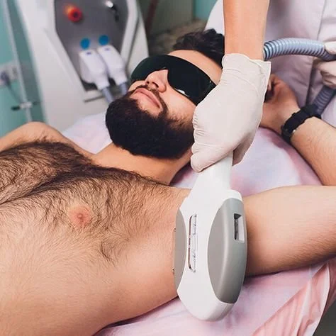 A man lying on a hospital bed undergoing a medical procedure with a technician applying a device to his chest, wearing a protective eye mask and a glove.