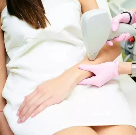 Medical procedure involving a person receiving laser treatment on their wrist done by a technician wearing pink gloves.