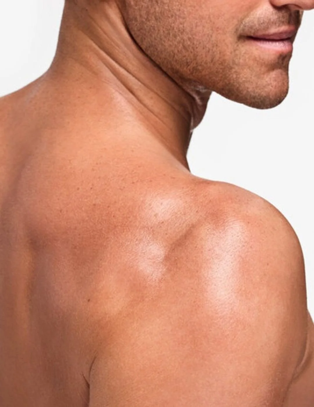Close-up of a shirtless man's shoulder, neck, and part of his face with light skin and stubble. The background is plain white.