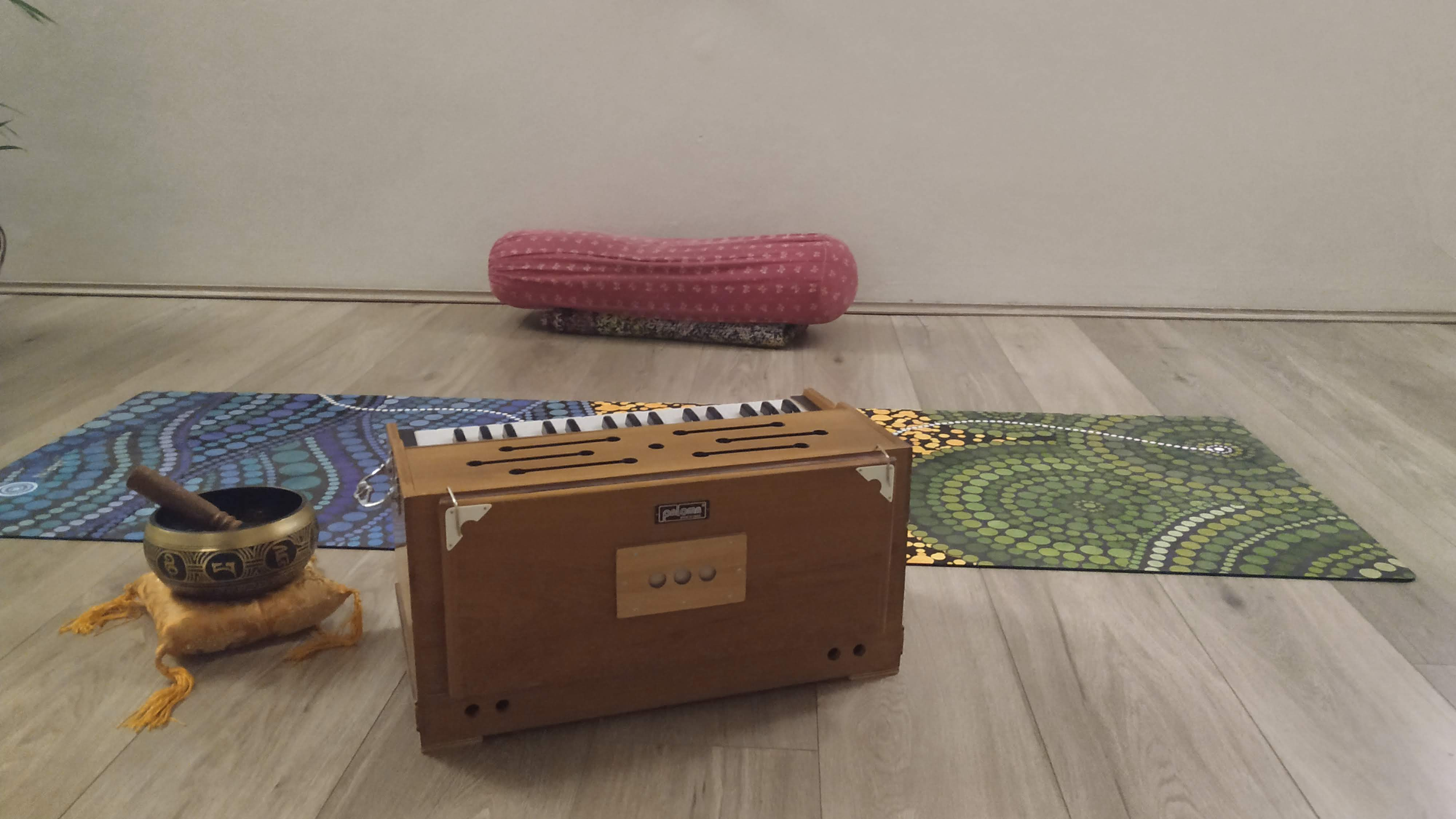 A harmonium, Tibetan prayer bowl, yoga mat and pink bolster sit in a yoga studio.