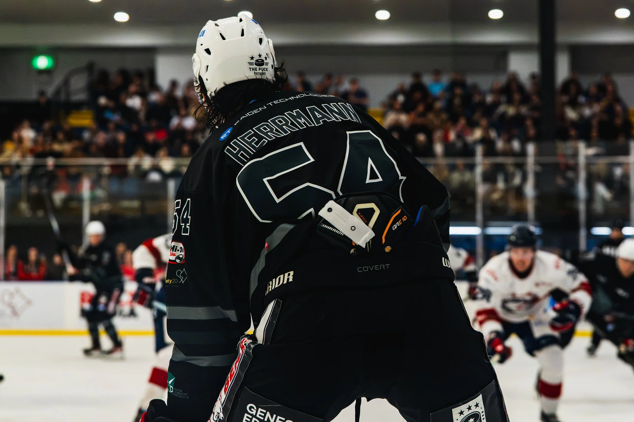 Ice hockey player wearing black jersey and white helmet with crowd in the background.