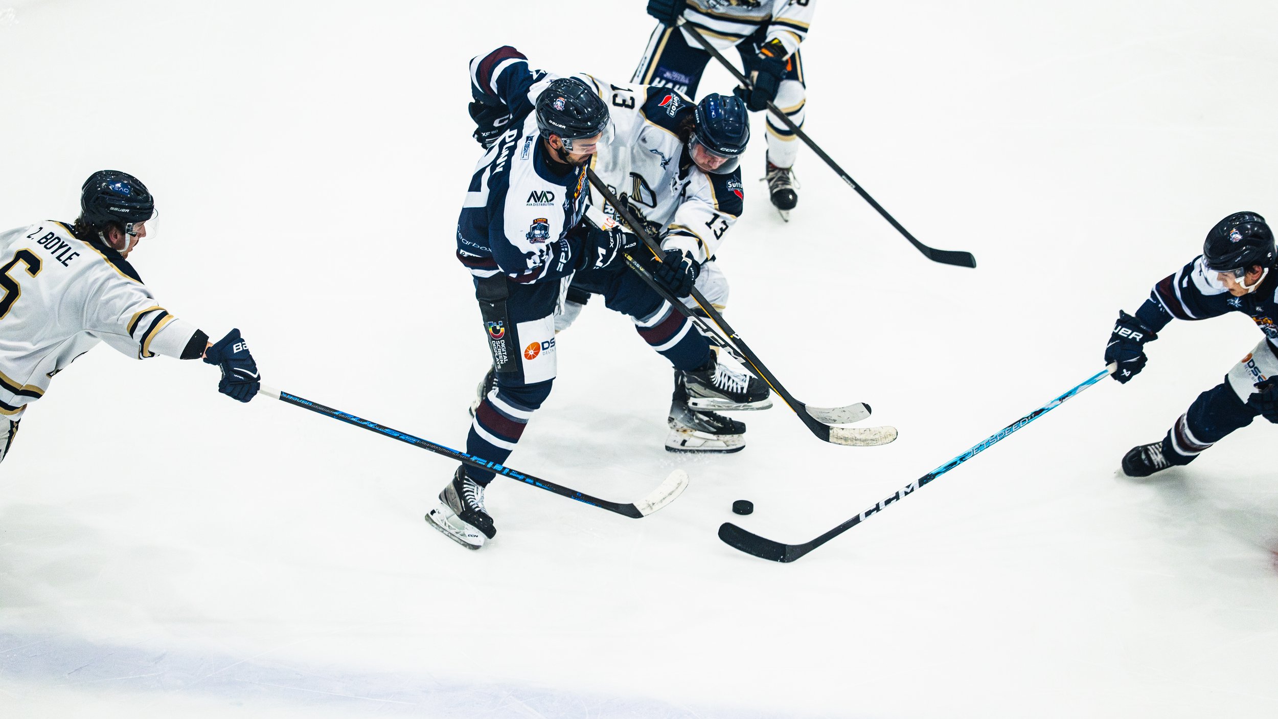 Ice hockey players from opposing teams competing for control of the puck during a game, on an ice rink.