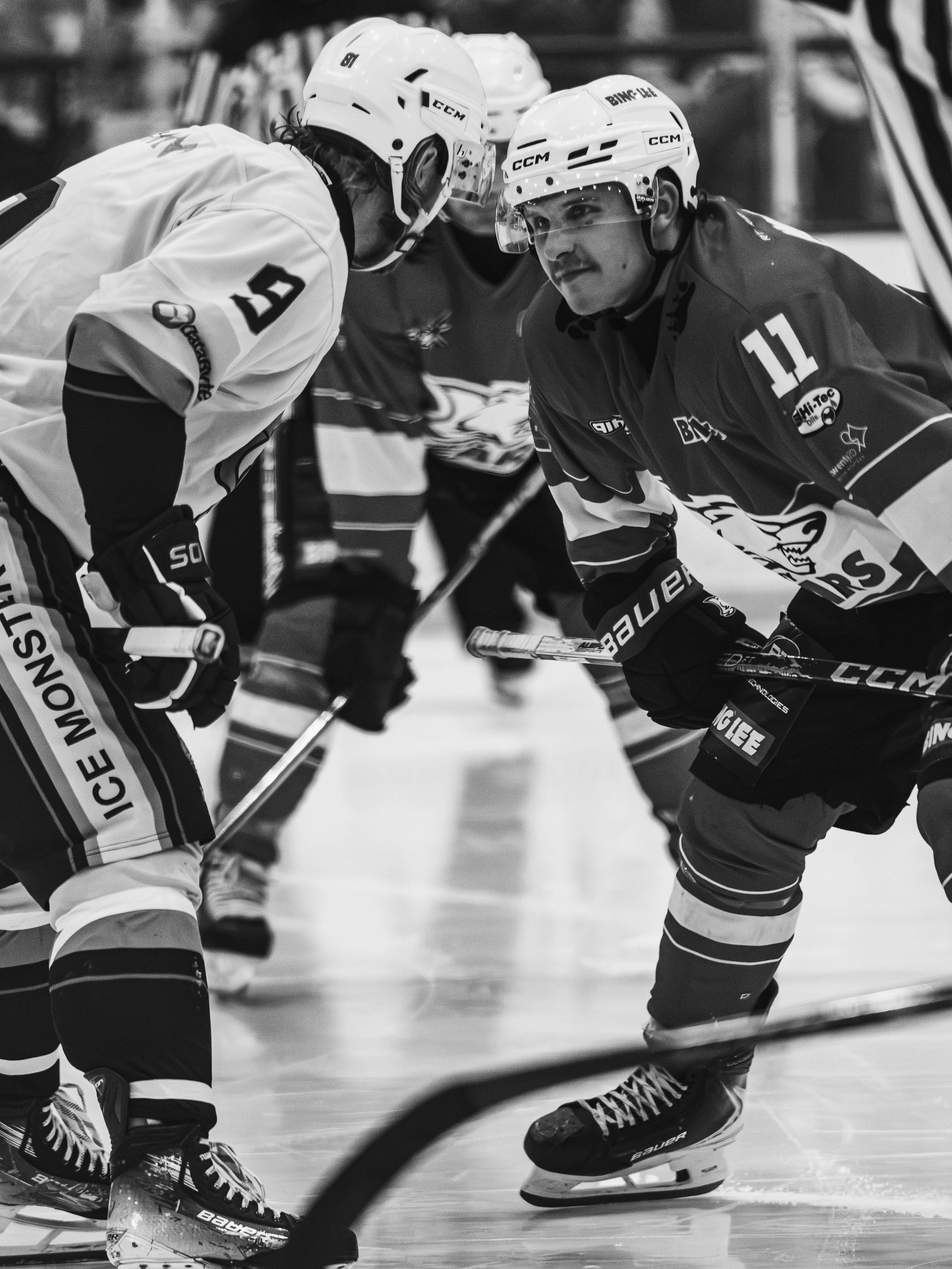 Two ice hockey players wearing helmets and protective gear are in close proximity, likely during a game or practice on the ice rink.