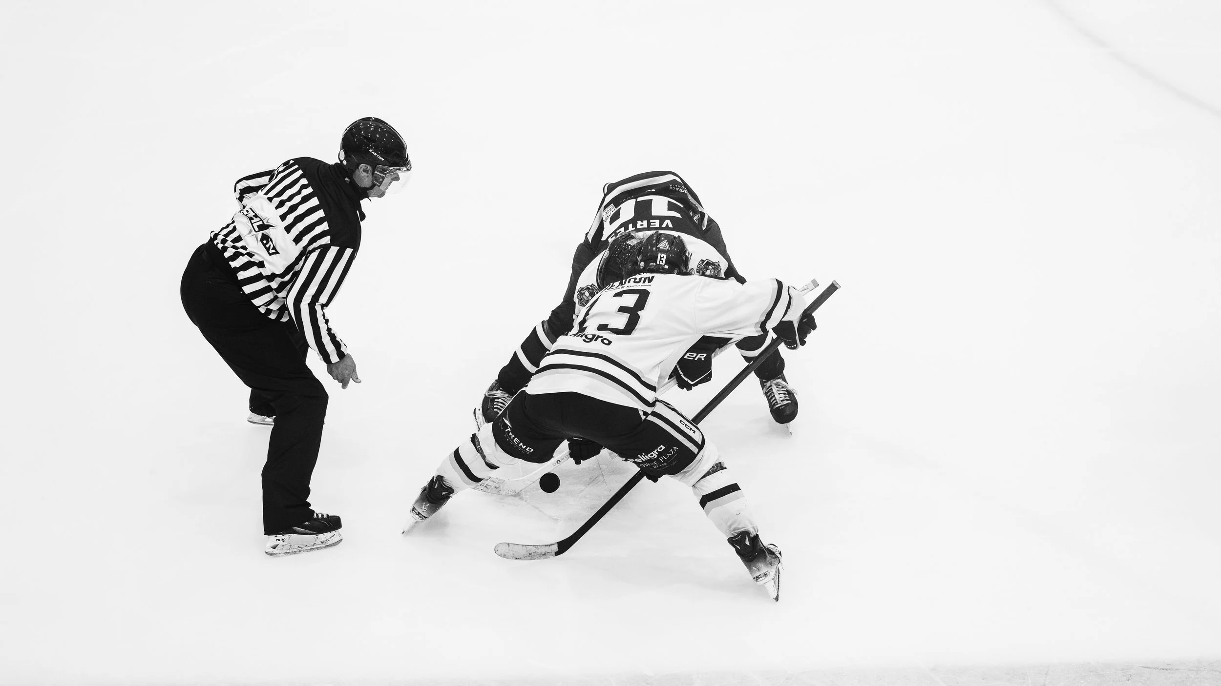 Ice hockey players and a referee involved in a puck confrontation on the ice rink.