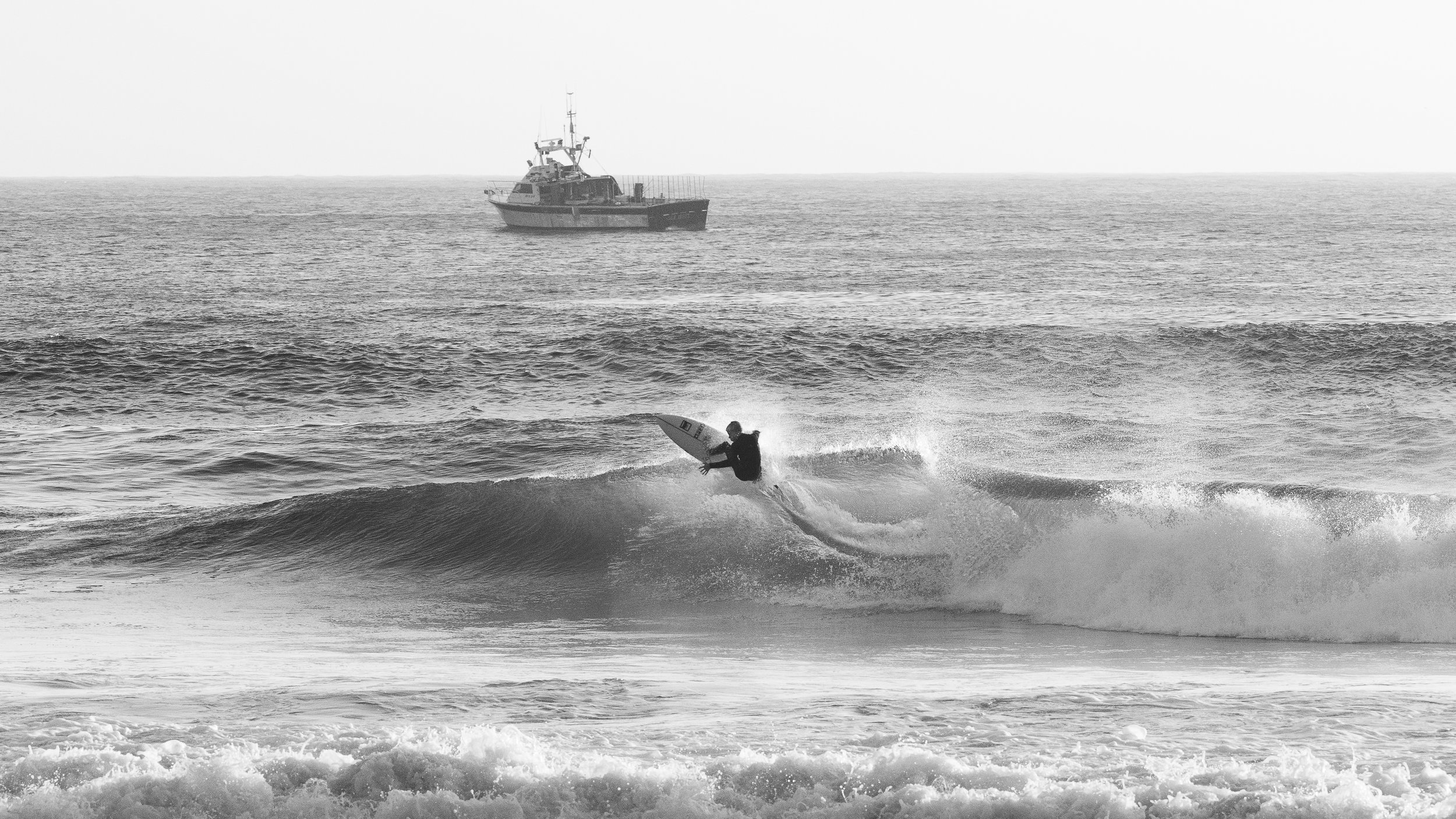 A person surfing on a wave with a boat in the background on the ocean.