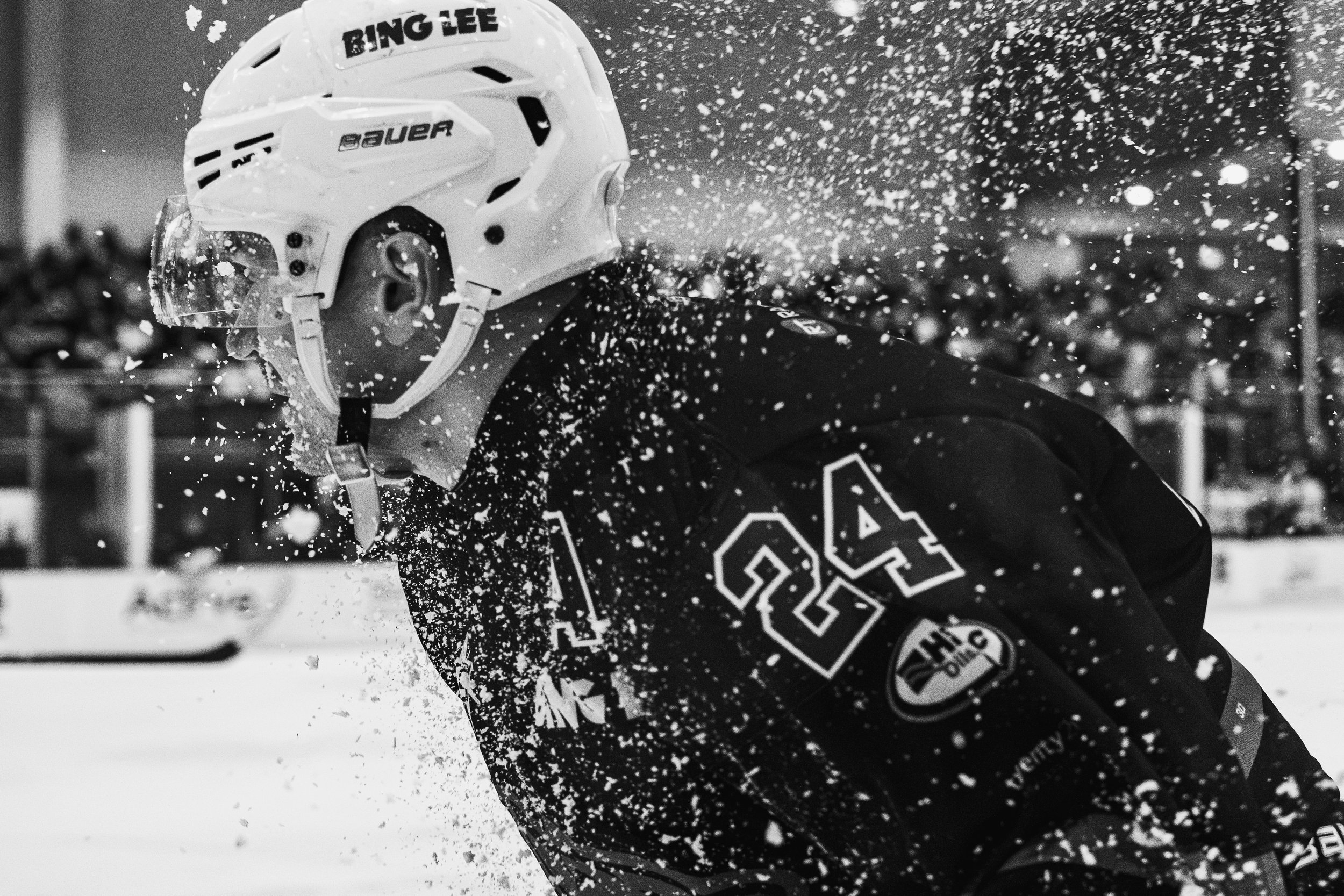 A hockey player in a helmet and jersey, with the name "Bing Lee" on the helmet, during a game or practice. The image is in black and white, with snow or ice particles flying around.