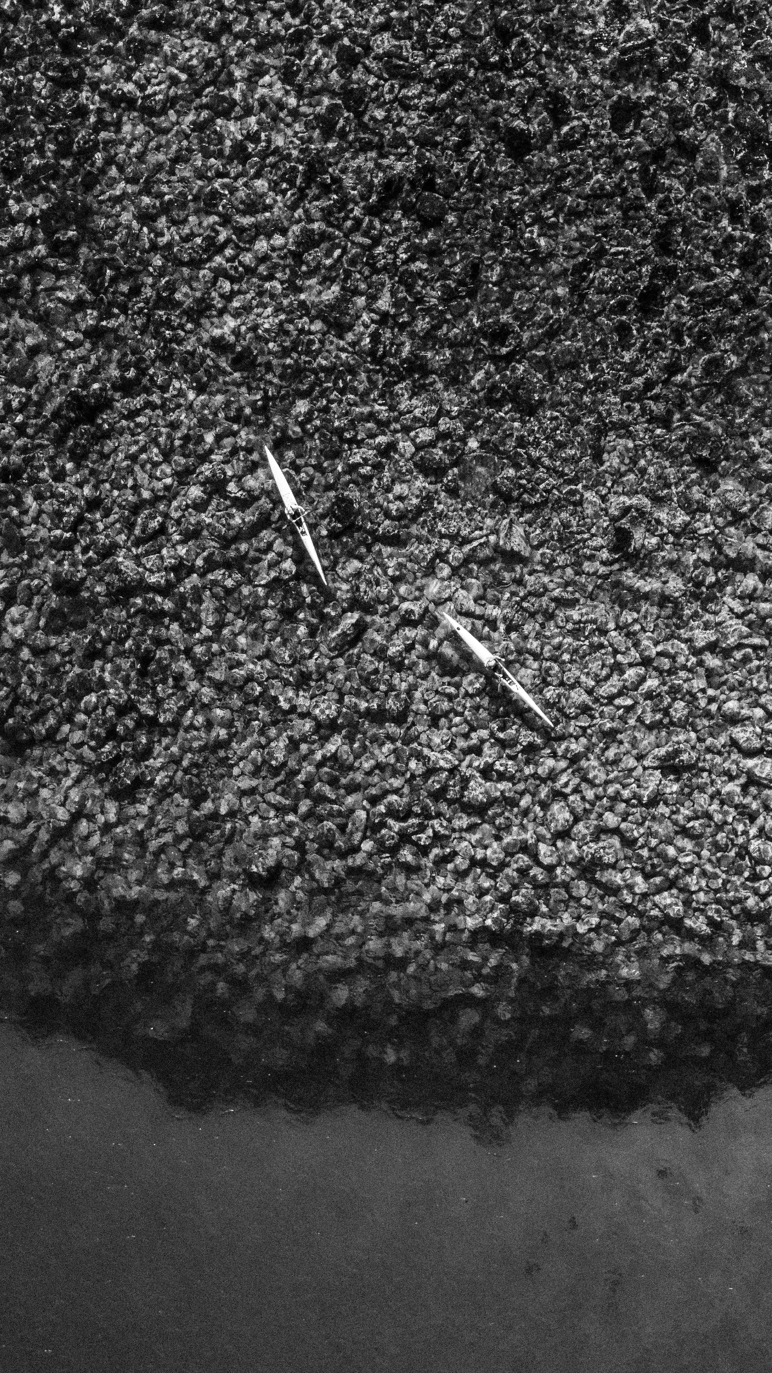 Two knitting needles embedded in a pile of small black rocks or gravel, with a black background.
