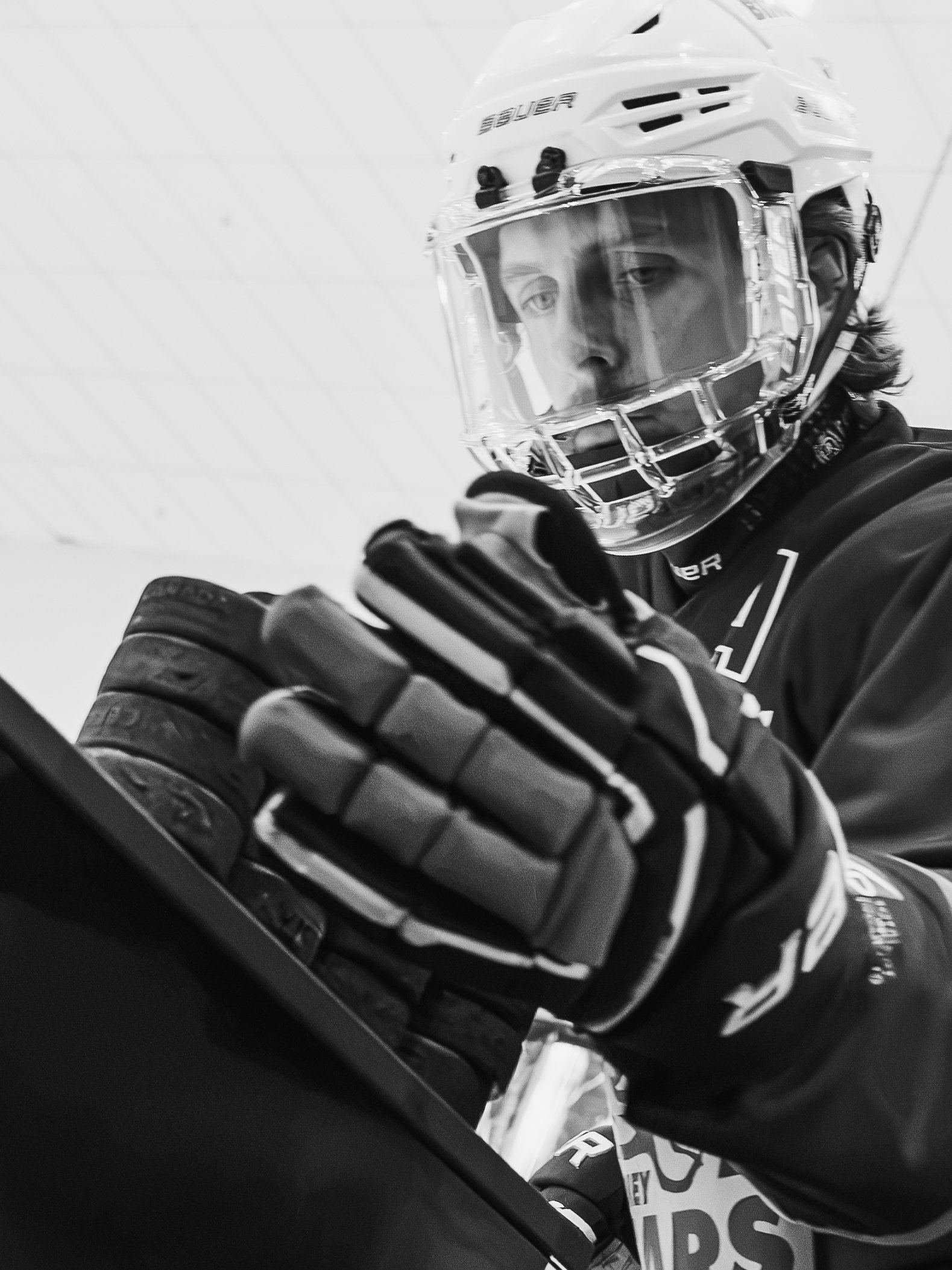 Close-up of a hockey player wearing a white helmet with a face shield, black gloves, and a jersey with letterings, on an ice rink.