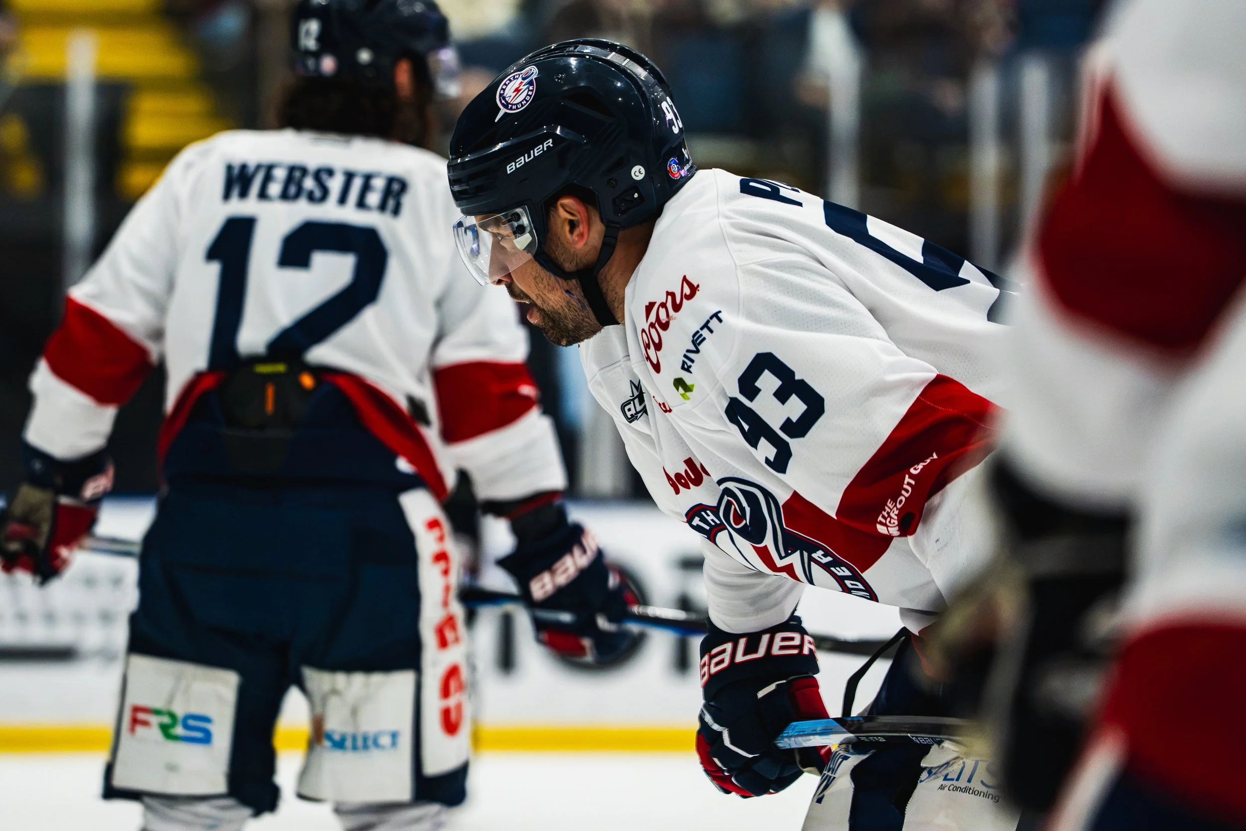 Ice hockey players on the ice during a game, focusing on one player wearing a black helmet and white jersey with the number 93, engaged in a moment of play.