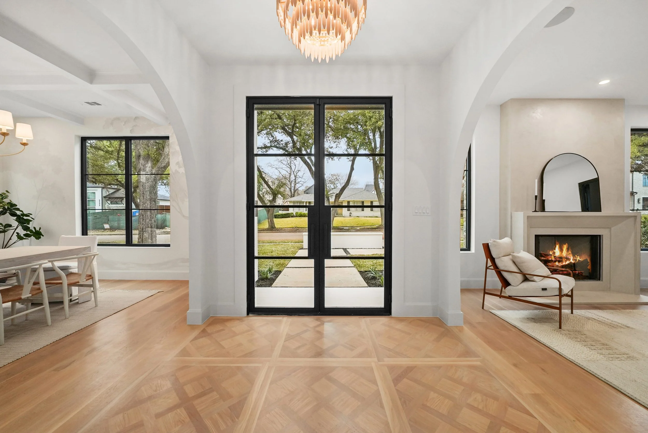 Modern living room with large glass double doors leading outside, white walls, a chandelier, fireplace, and seating area.