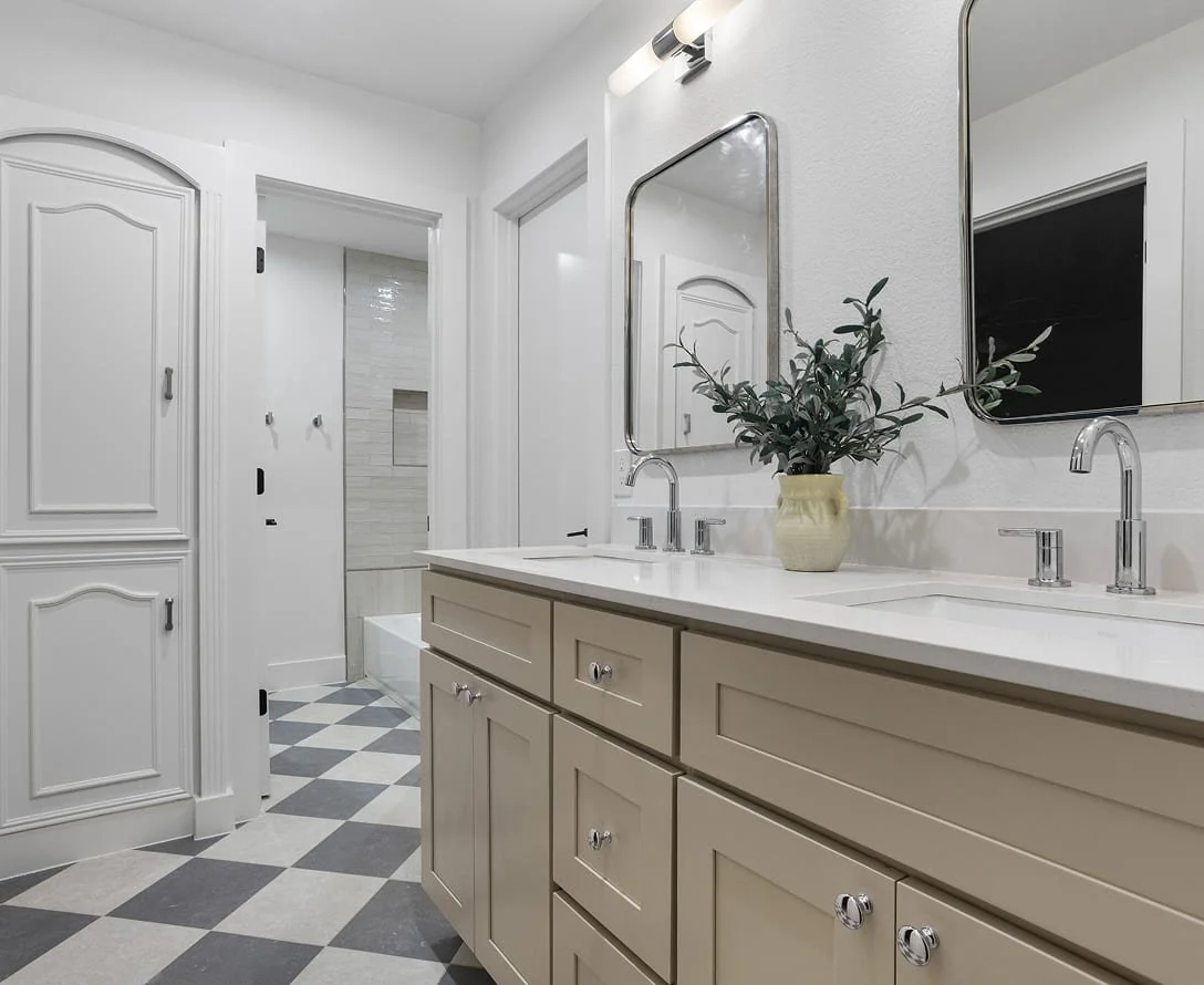 Bathroom with a double vanity, large mirrors, a potted plant, and a walk-in shower with tiled walls.