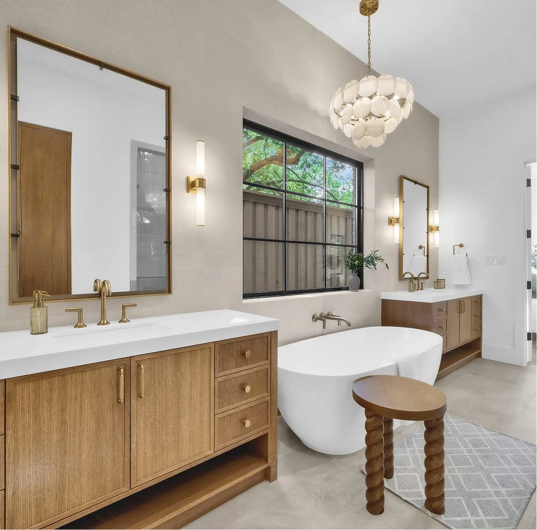 Modern bathroom with wooden vanities, white freestanding bathtub, large window, and stylish pendant and wall lights.