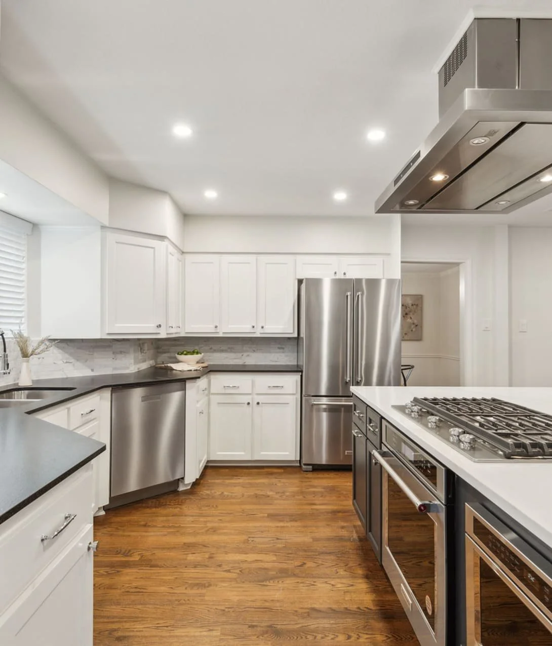Modern kitchen with white cabinets, stainless steel appliances, and wood flooring.