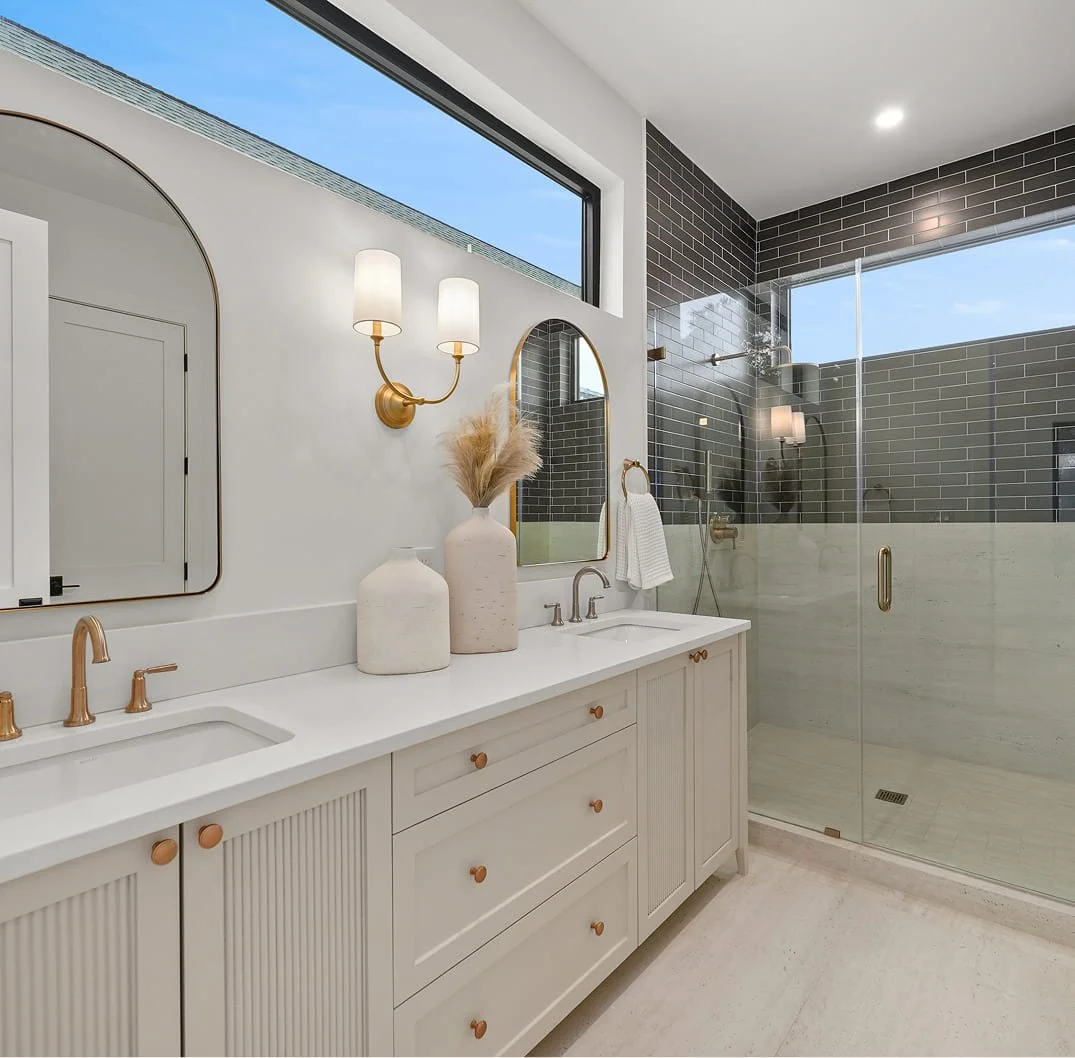 Modern bathroom with a double vanity, gold fixtures, and a walk-in shower with black subway tiles and glass enclosure.