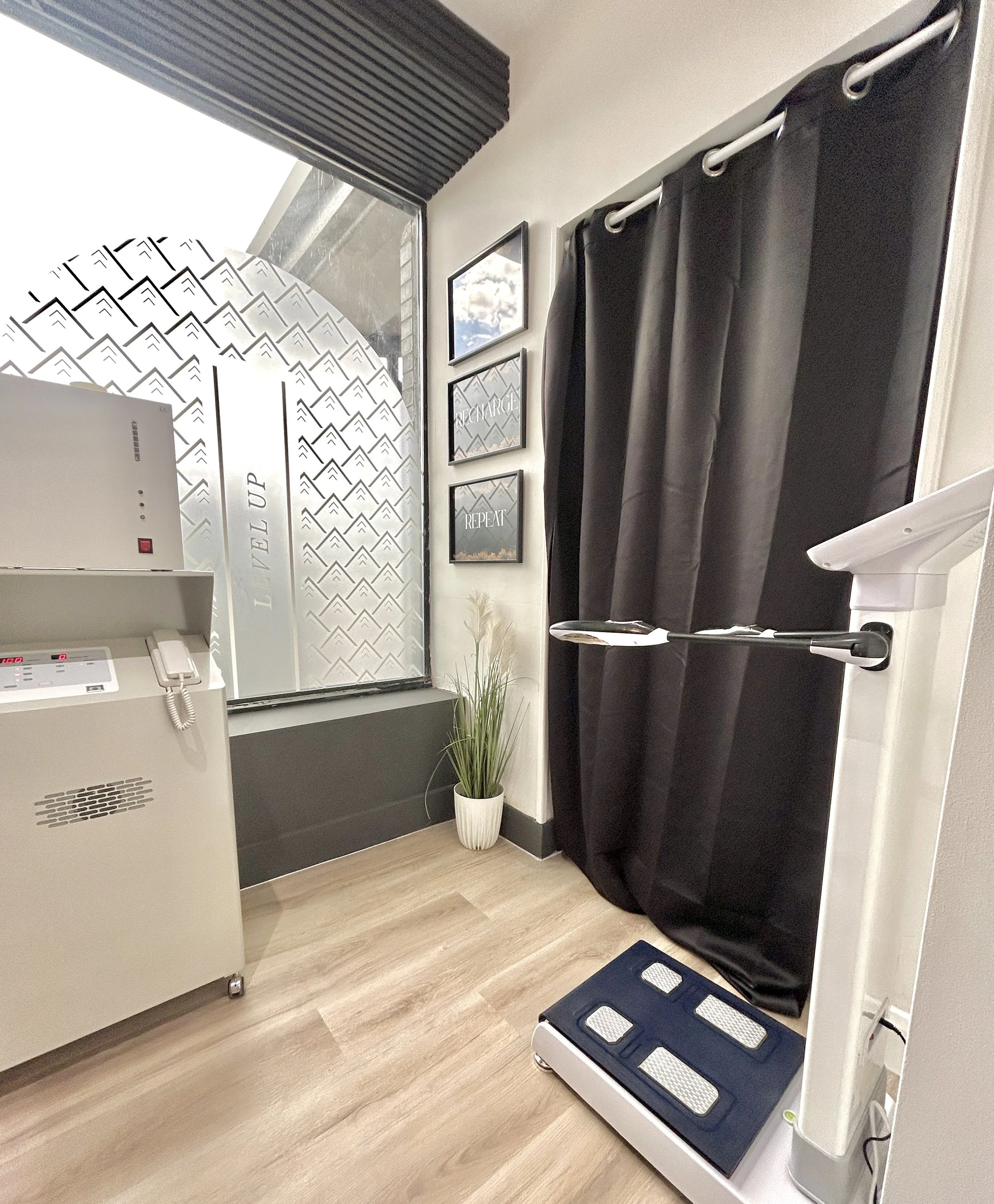 Interior of a clinic or medical facility with a window, framed inspirational quotes on the wall, a potted plant, a sterilizer, and a step stool near a white appliance.