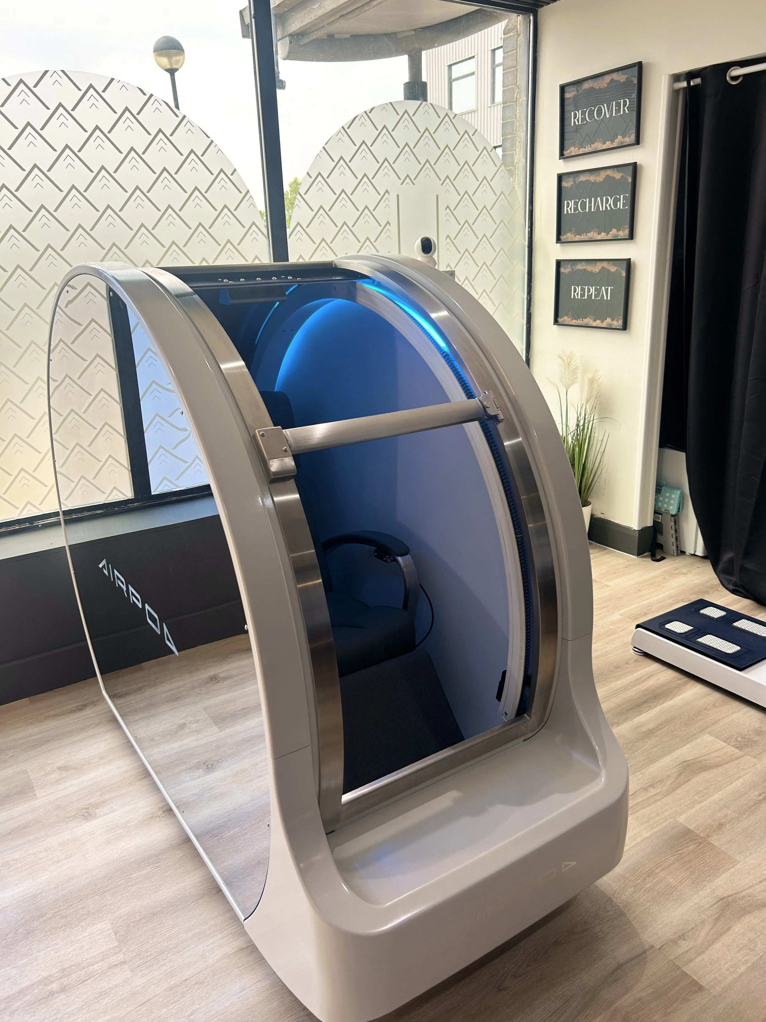 A modern hyperbaric oxygen therapy chamber in a room with wood flooring, windows, and motivational wall art.