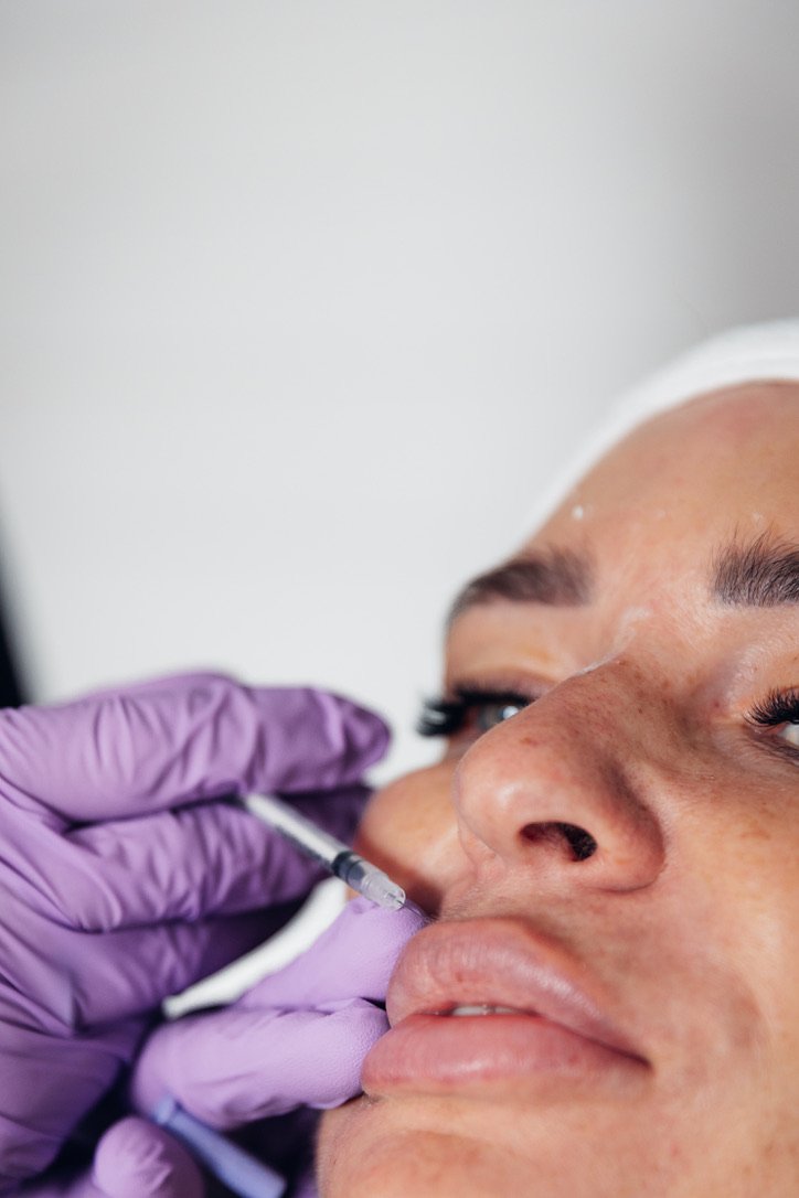 A nurse practitioner performing lip filler treatment on a female patient to enhance lip shape