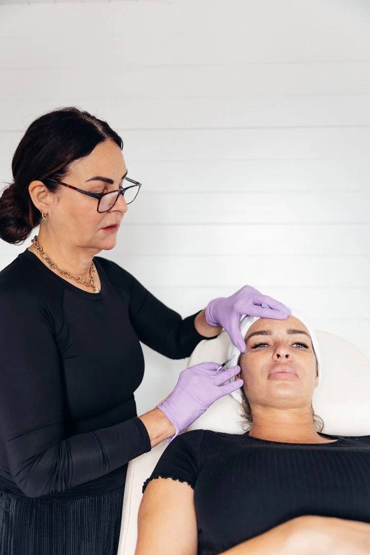 A female nurse practitioner injecting dermal filler into a female patient for more volume and skin definition at a modern clinic in Broadstone