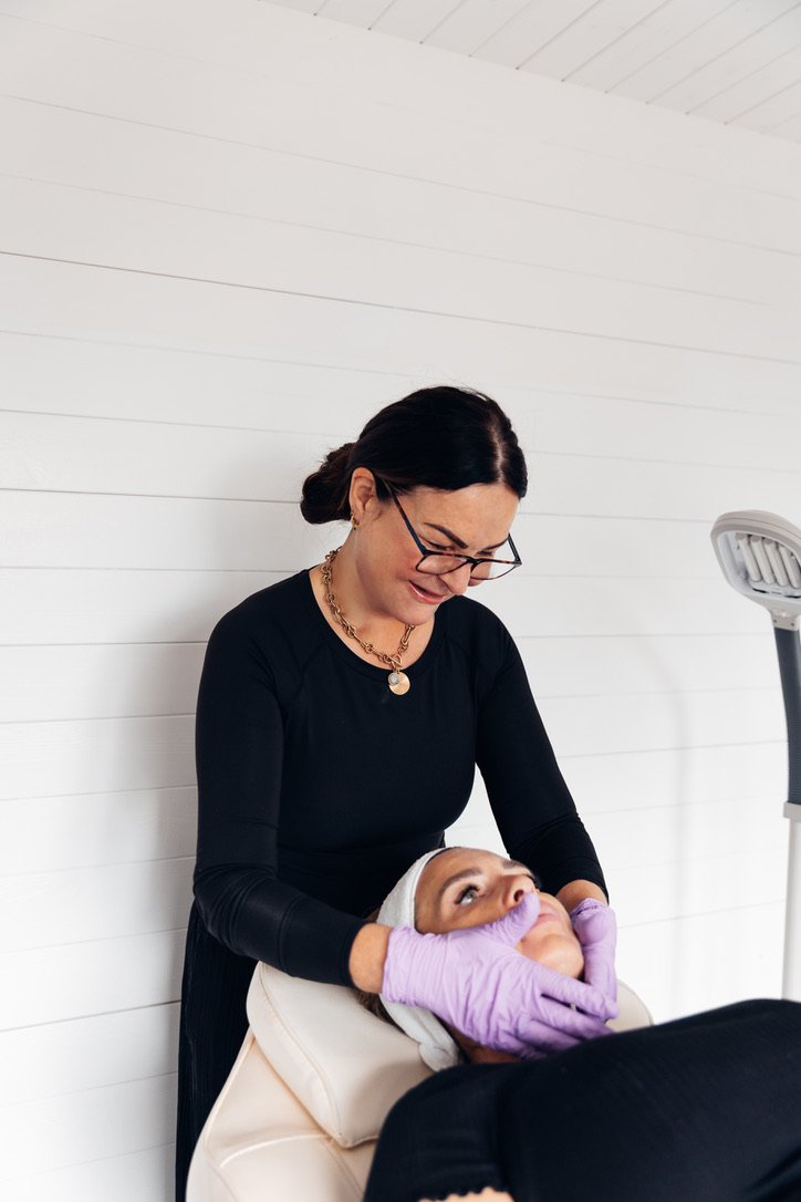 A woman receiving a facial treatment from a skincare professional wearing purple gloves at a spa or skincare clinic.